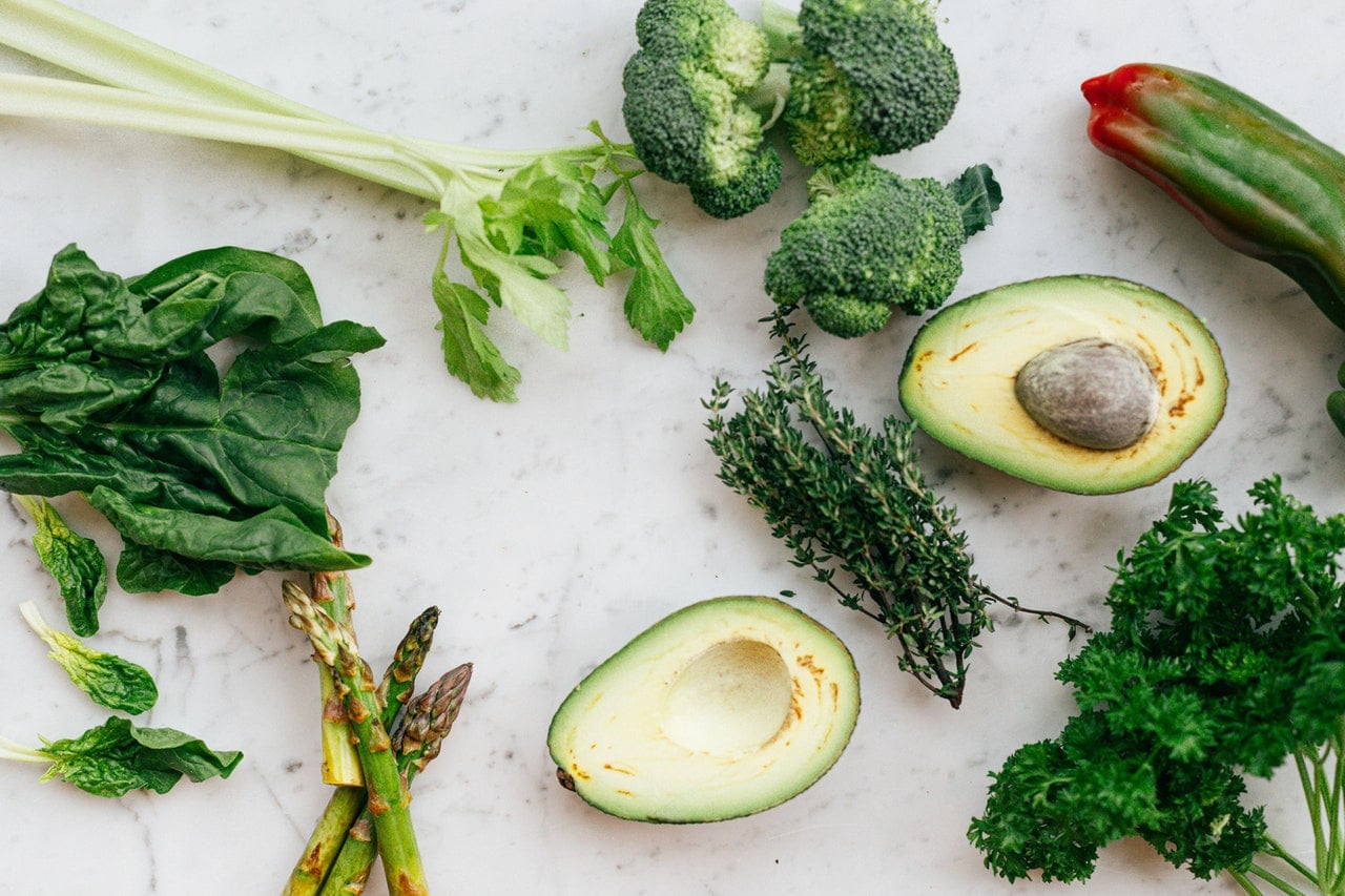 Grünes Gemüse wie Spinat Brokkoli Avocado und Spargel liegt verteilt auf weißem Untergrund