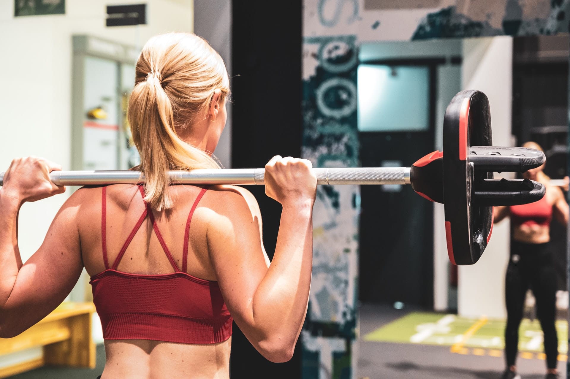 Eine Frau hebt Gewichte vor einem Spiegel im Fitnessstudio.
