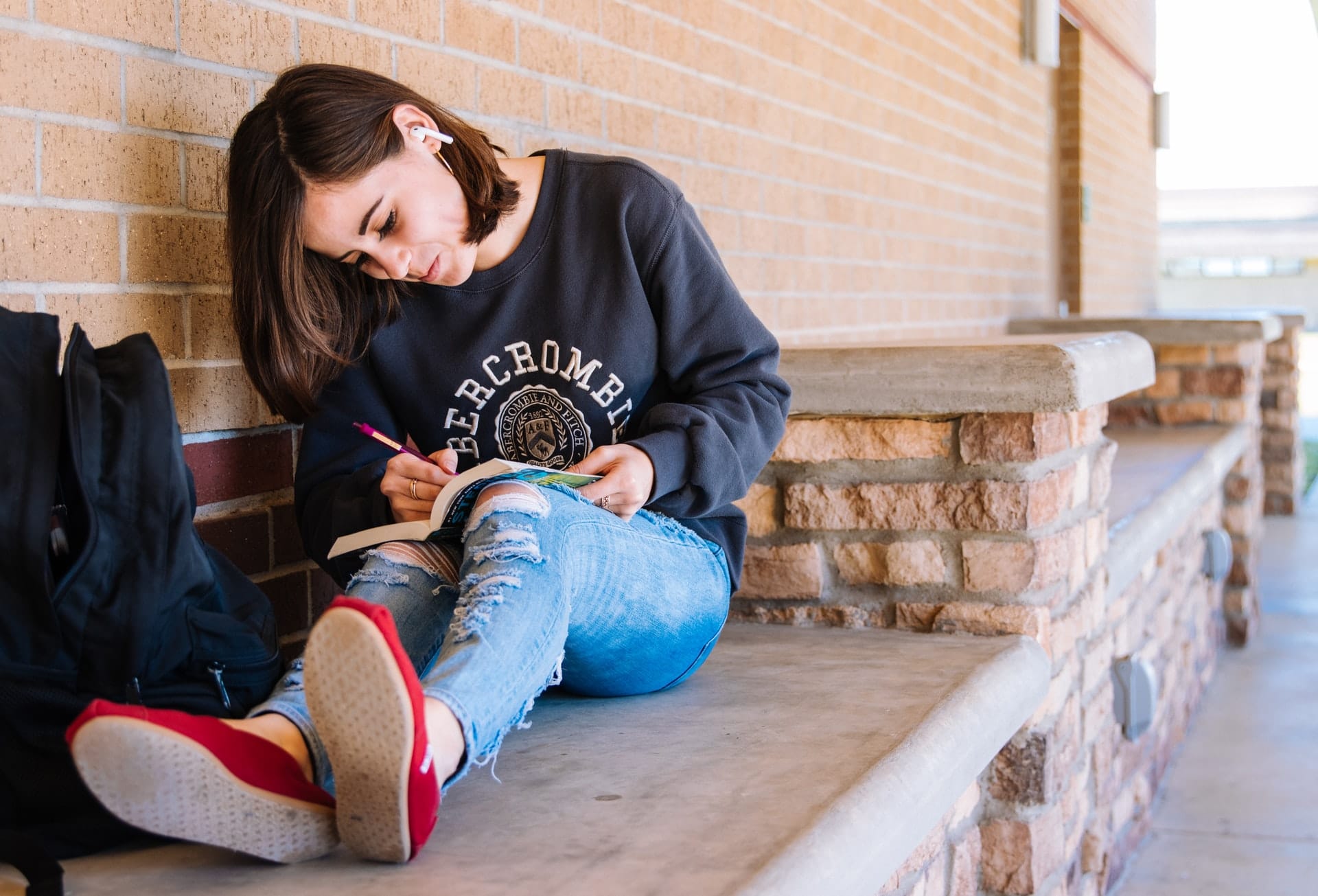 Mädchen mit braunen Haaren schwarzem Pulli und Jeans sitzt und schreibt in Buch