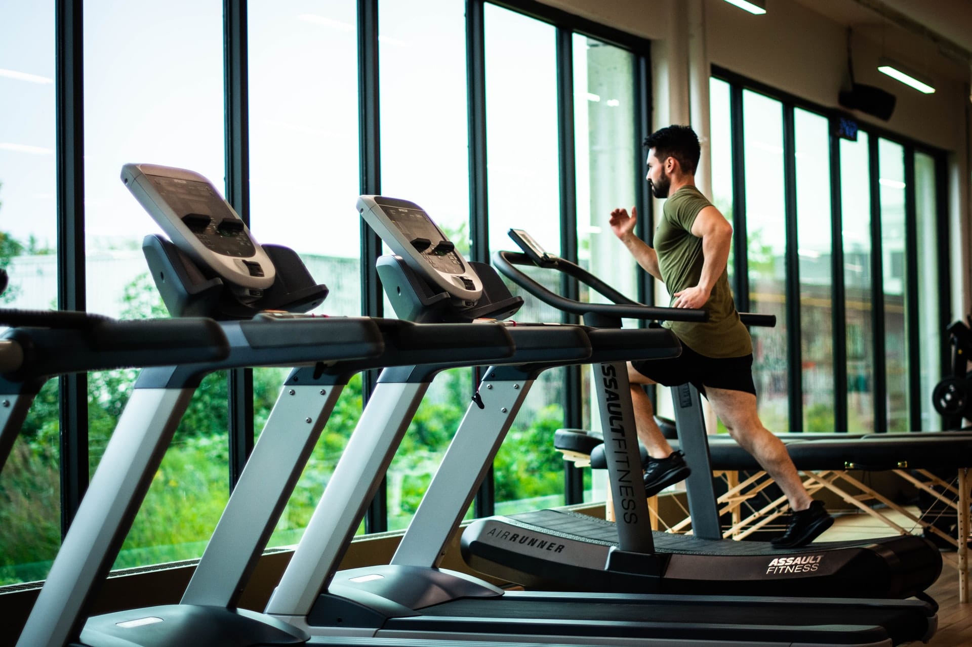 Ein Mann läuft im Fitnessstudio am Laufband neben einer Fensterfront.