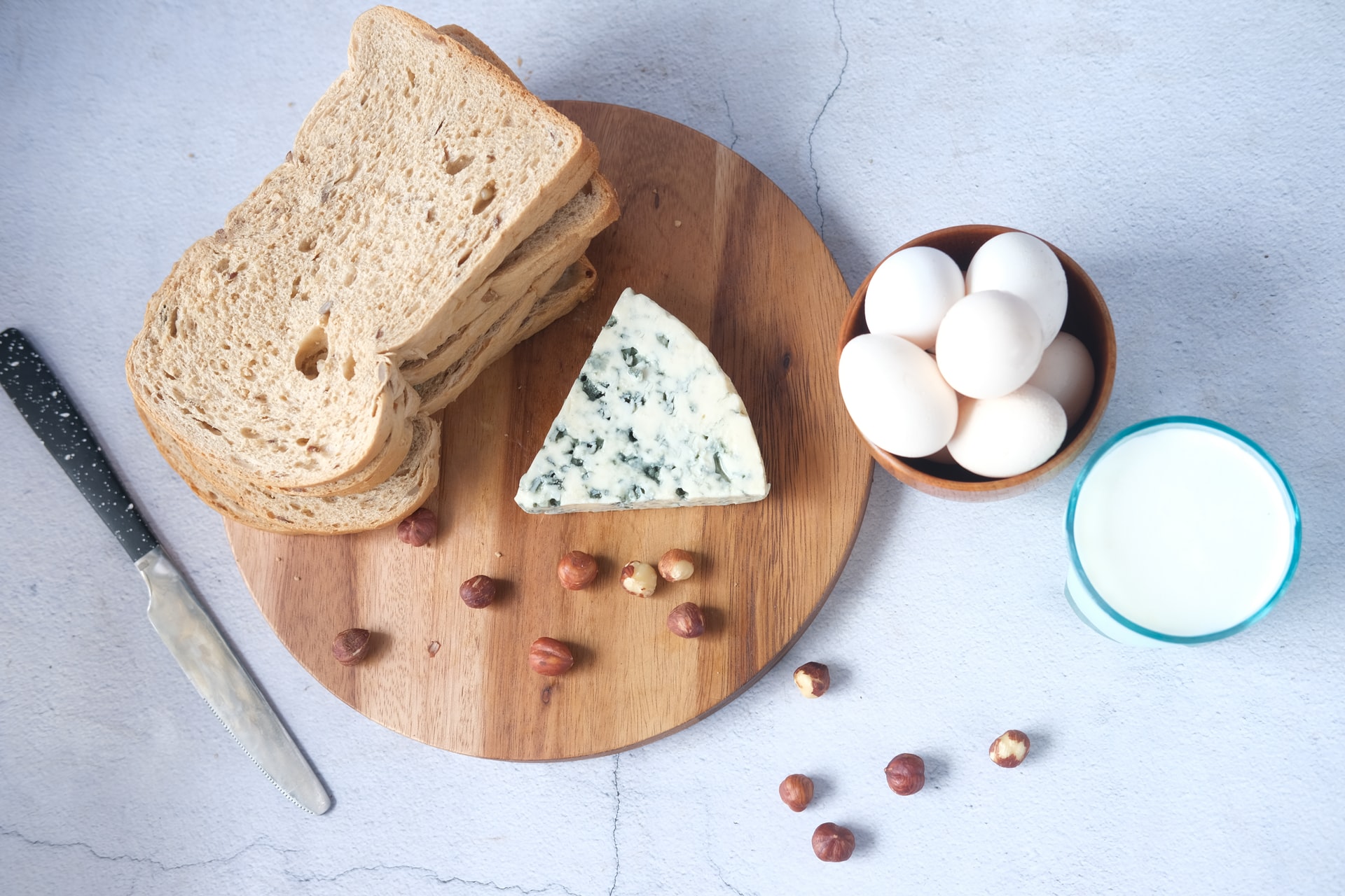 Brot Käse und Nüsse liegen auf Holzbrett daneben Eier und Milch