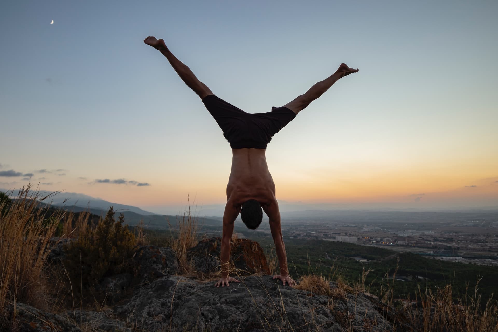 Mann ohne Shirt macht Handstand während die Sonne untergeht