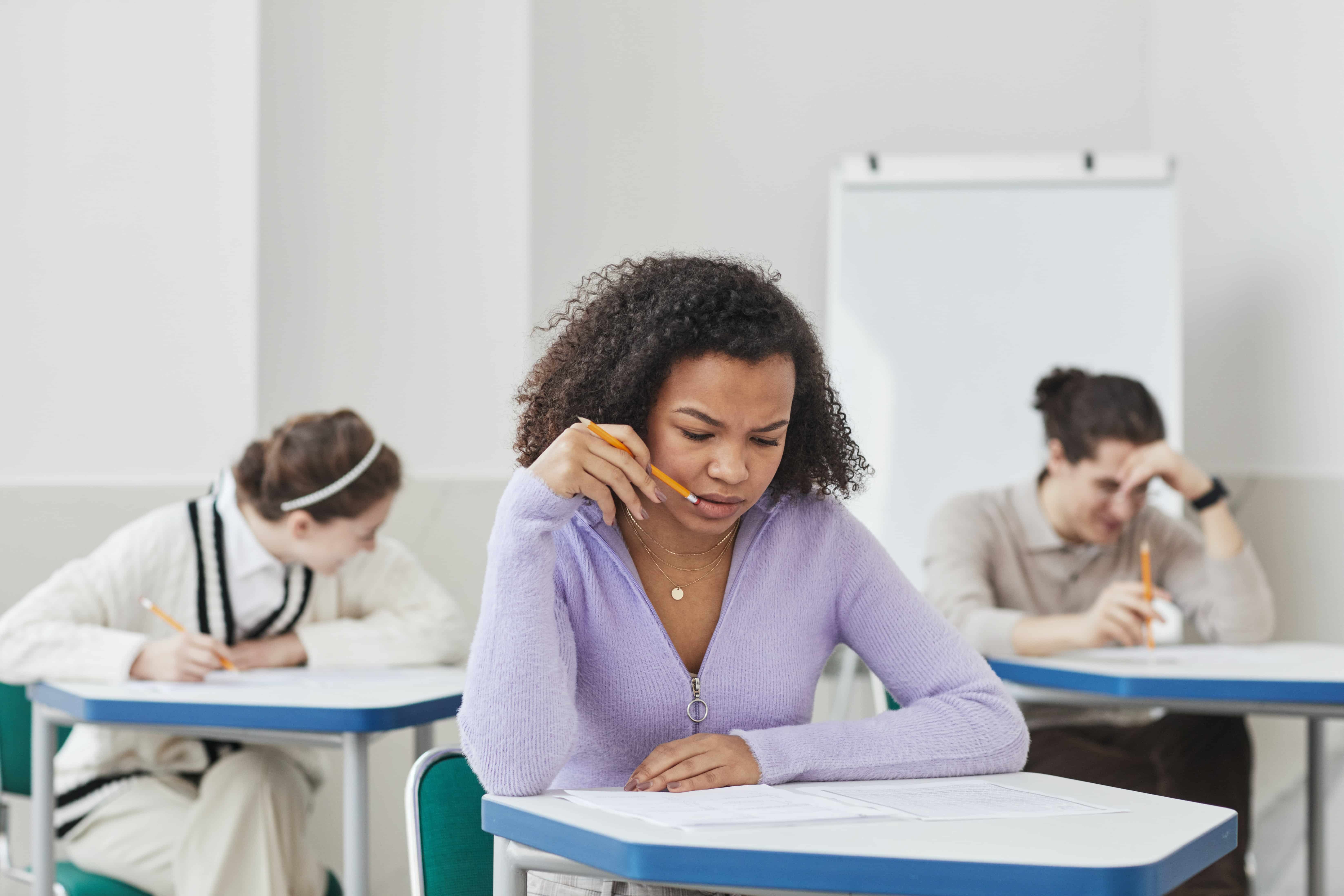 Mädchen mit dunklen Haaren und violetter Weste sitzt an Schulbank