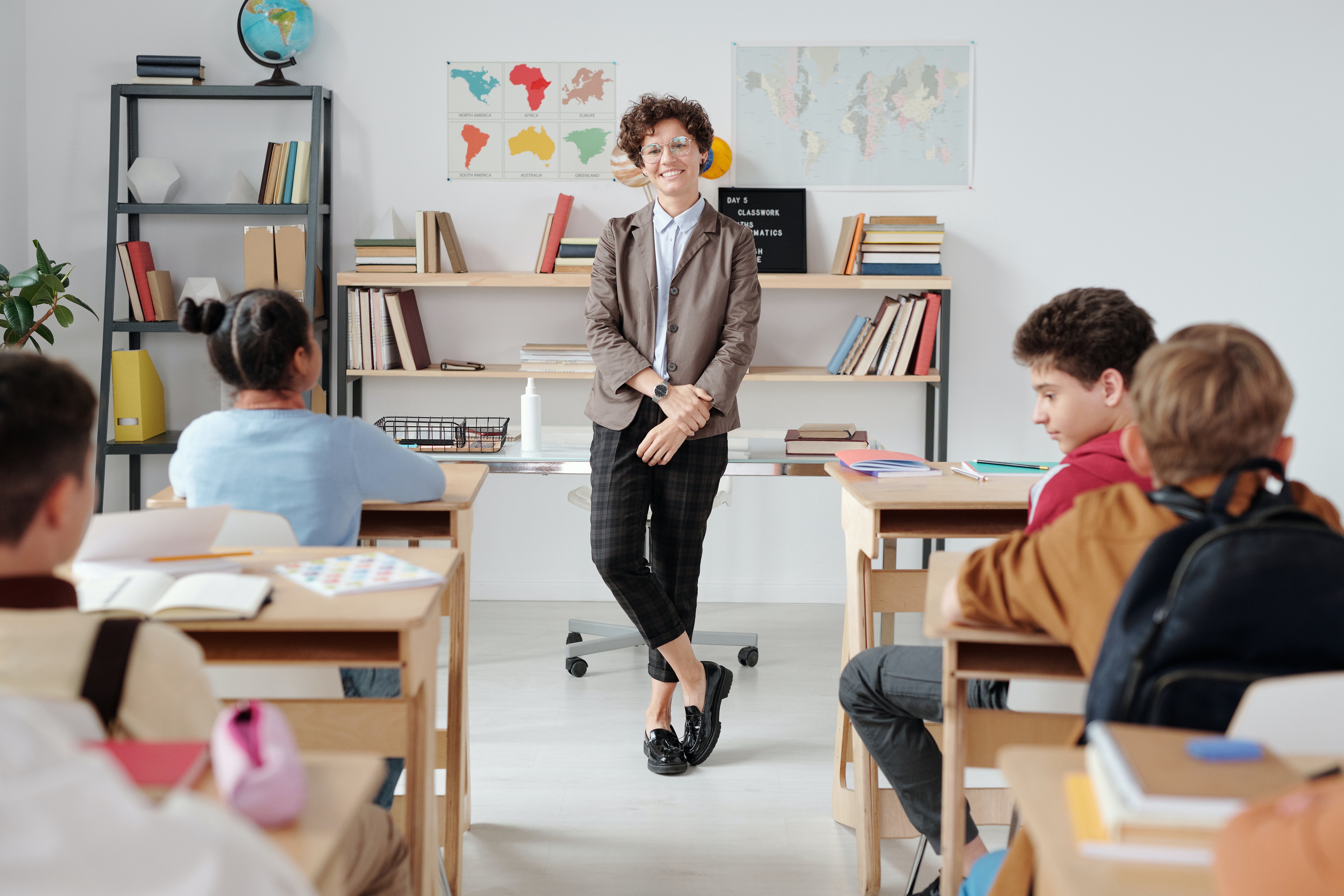 Lehrerin steht mit verschränkten Beinen vor Klasse