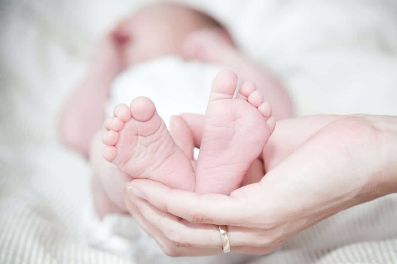 Baby liegt auf weißer Decke Person hält Füße