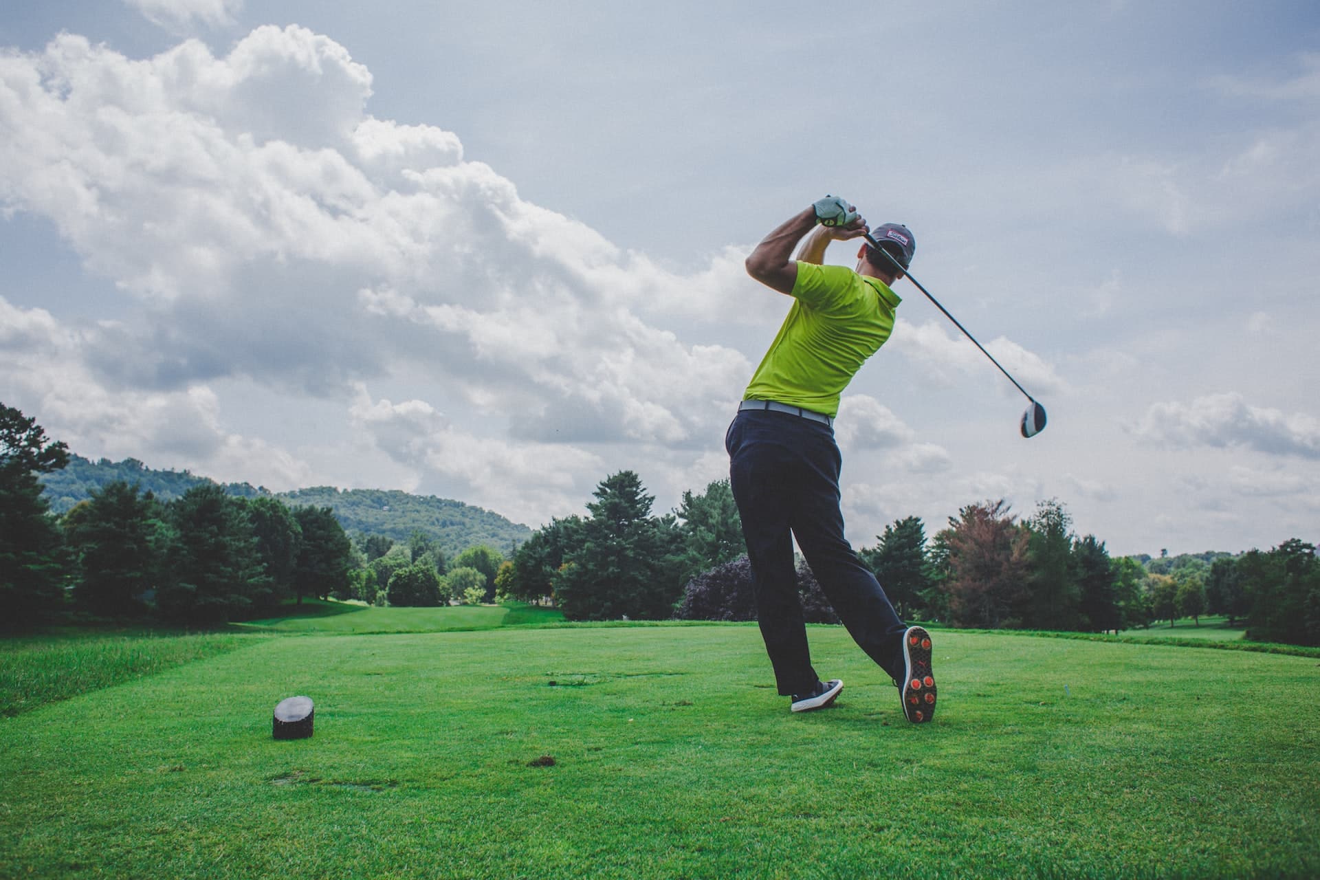 Ein junger Mann schwingt einen Golfschläger und schießt damit den Golfball am Feld weit weg.
