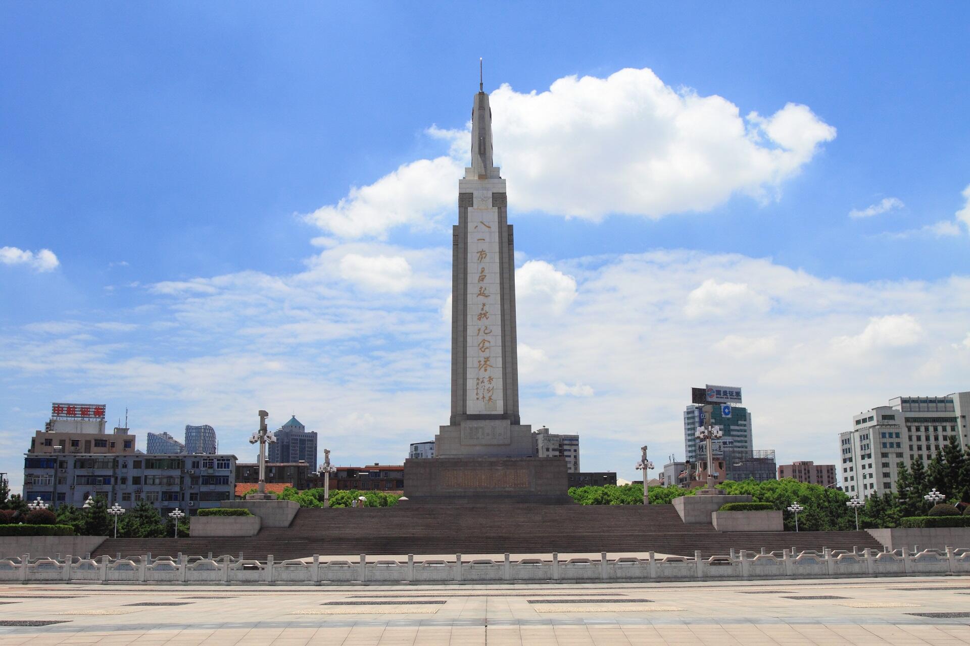A tall monument in a public square with golden Chinese writing on it.