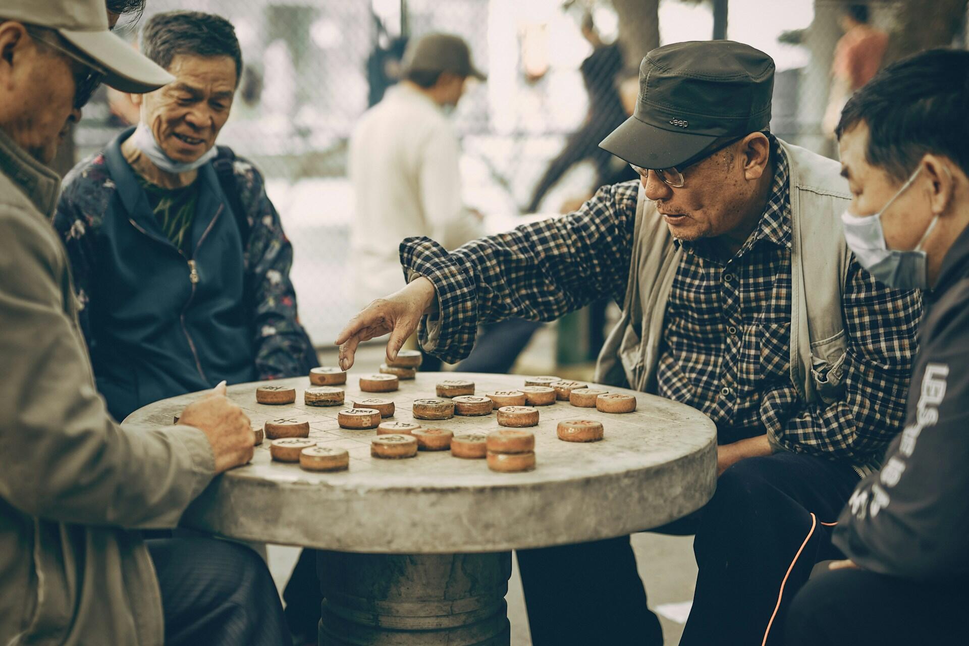 A group of old men sitting around a round table playing Chinese chess outdoors.