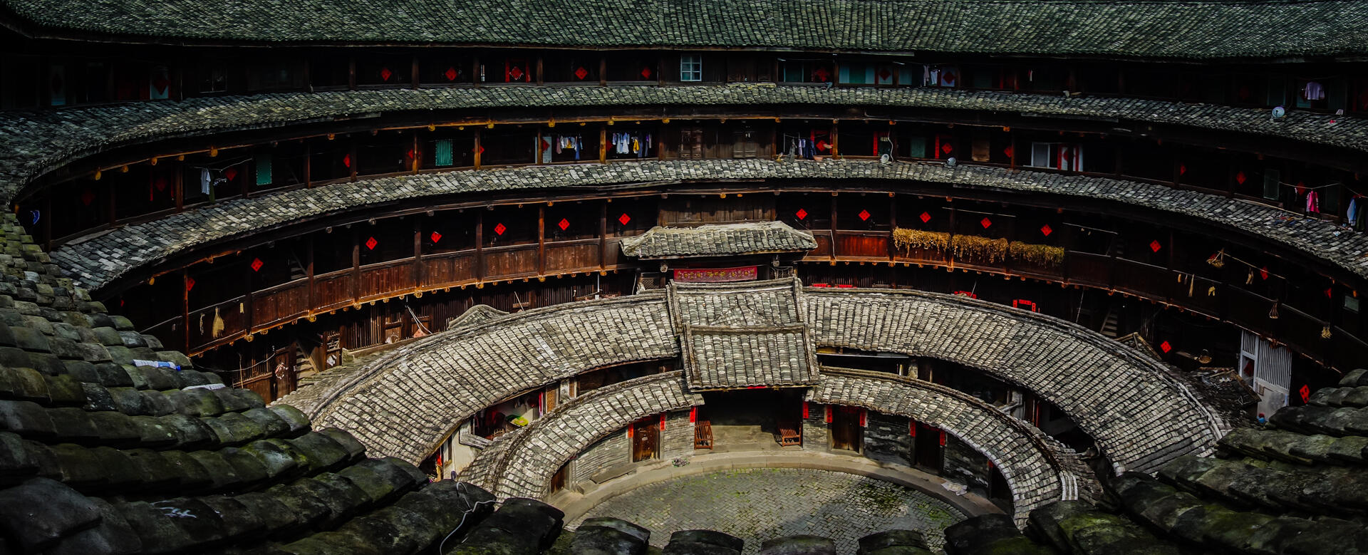 View of a circular, multi-story Fujian Tulou with tiled roofs and wooden balconies.