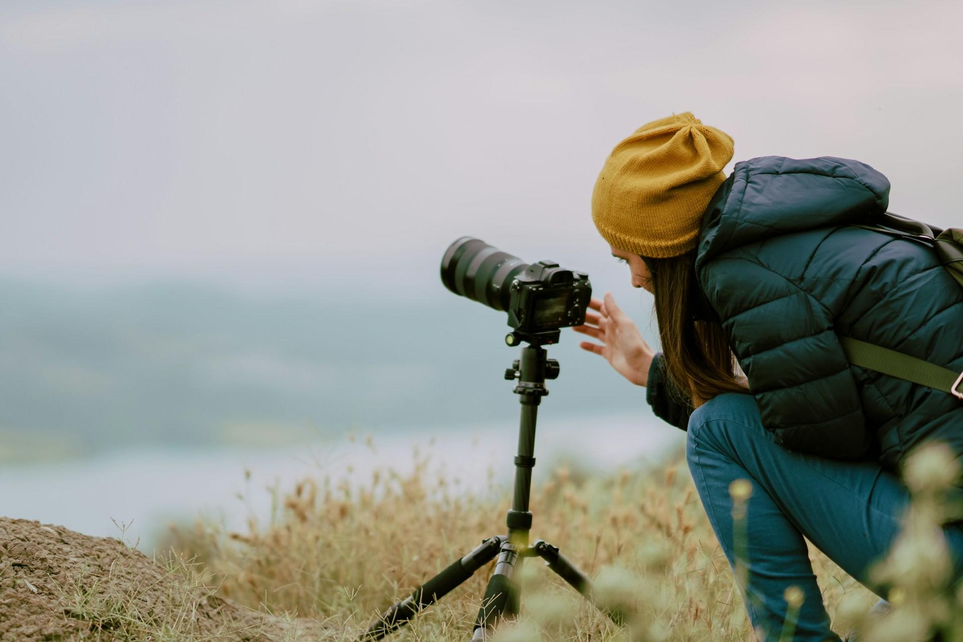 Person in a yellow hat adjusting a camera on a tripod outdoors.