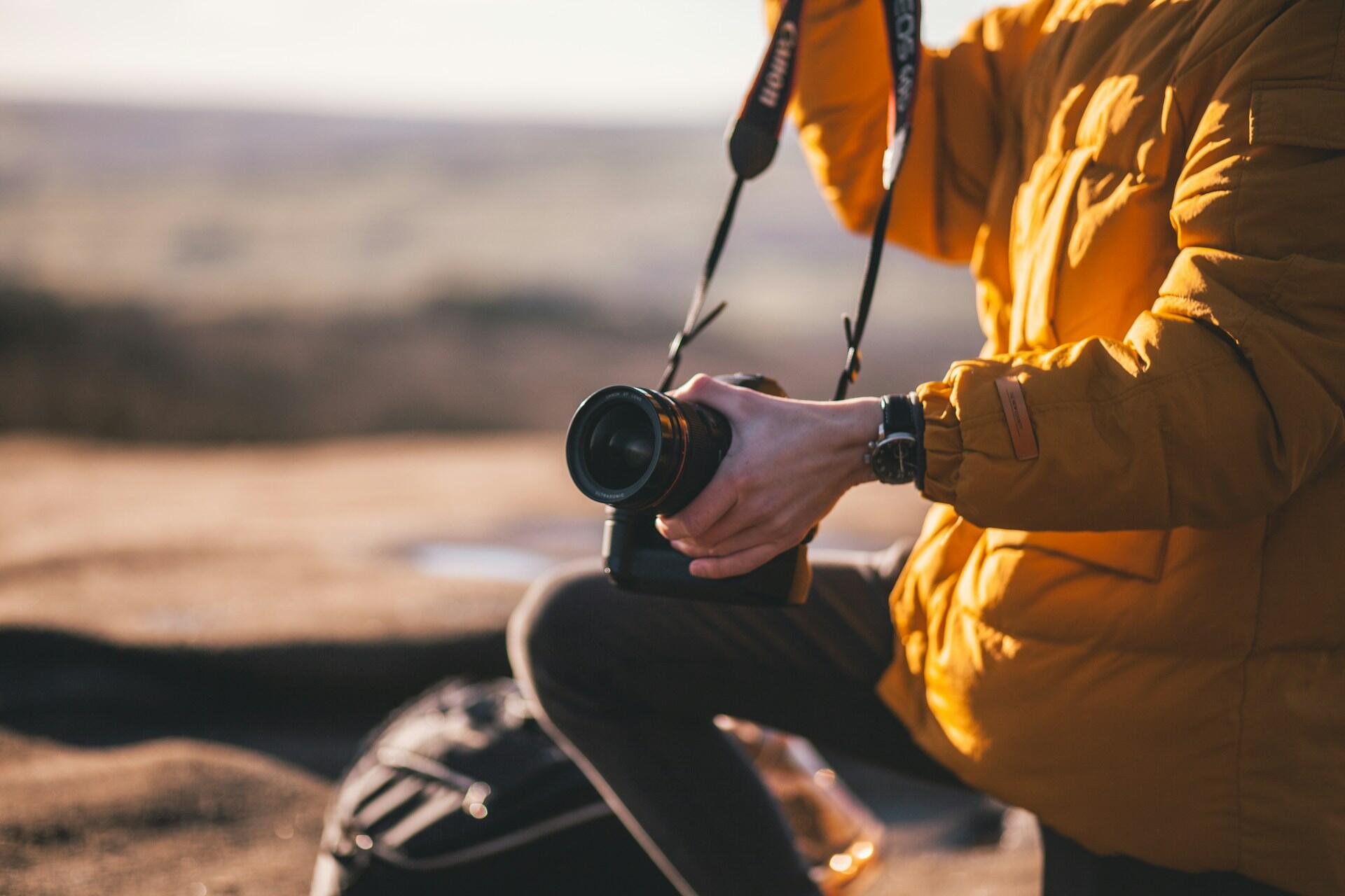 Person in orange jacket holding a camera outdoors at sunset.