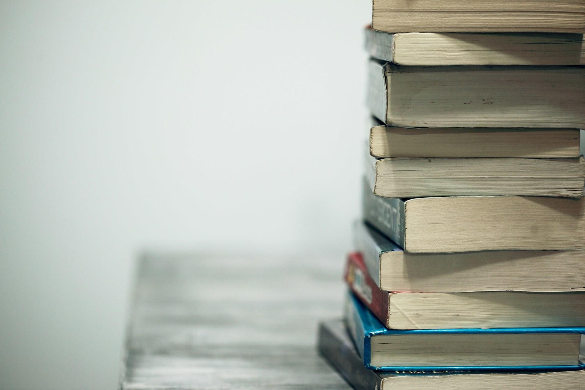 A stack of books, haphazardly arranged, fill the frame's right side while the picture's left side is left blank and white.