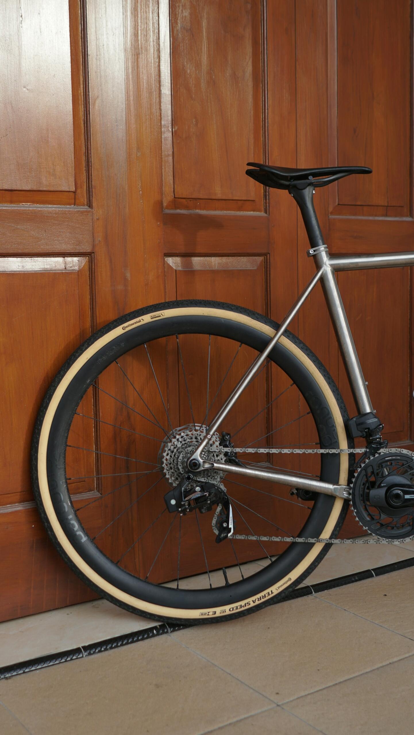 A silver bicycle's back wheel in front of a wooden door.