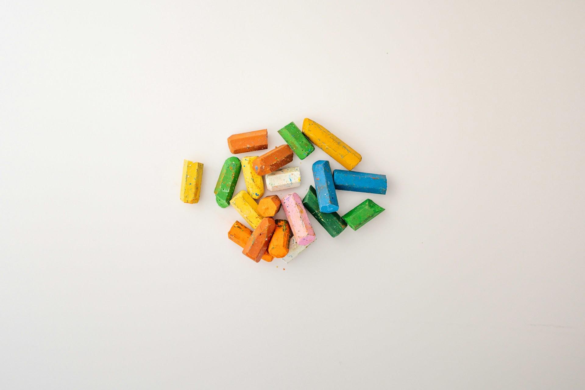 Some used colourful .chalks on a white surface