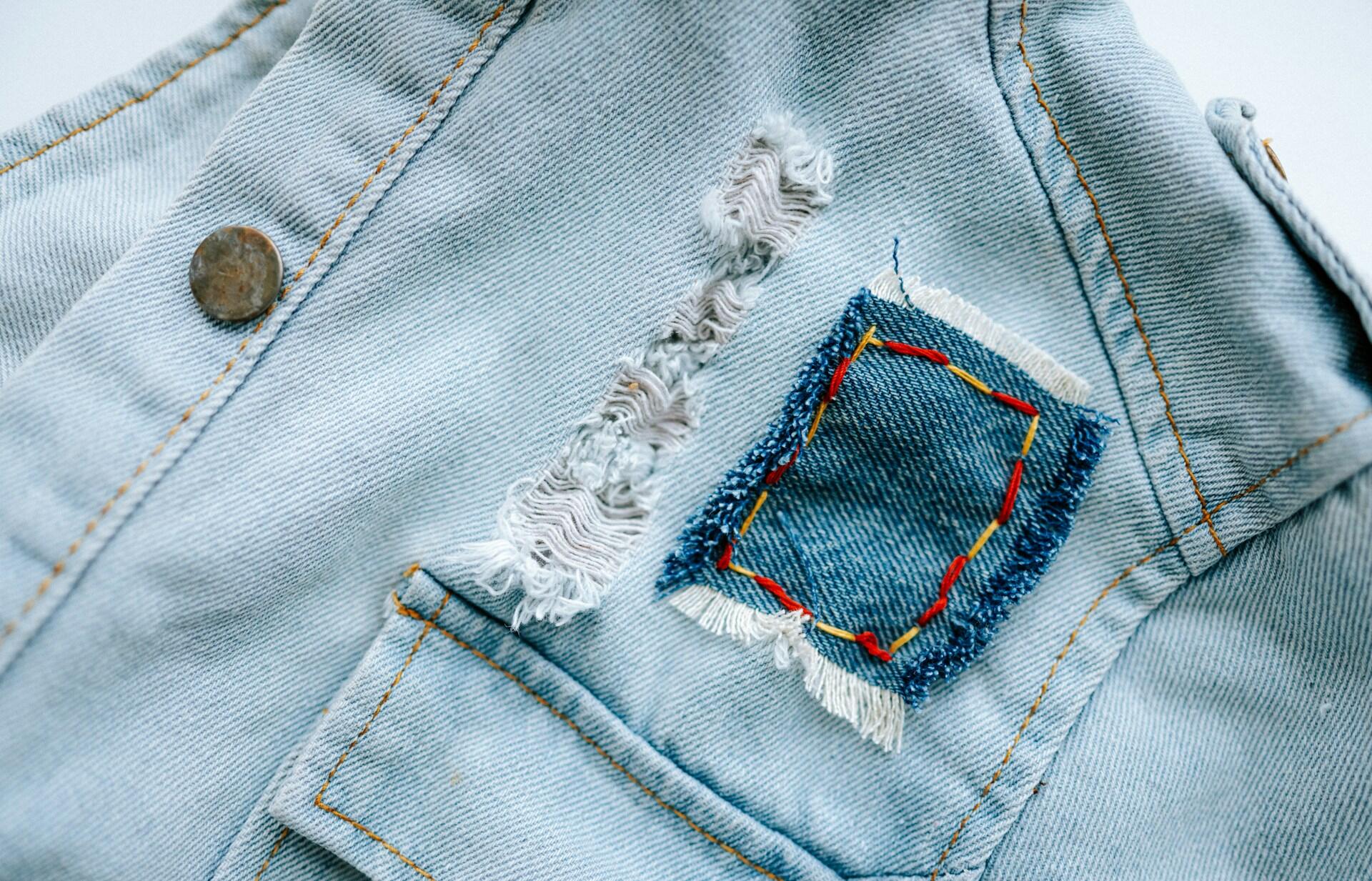 a denim jacket with functional straight stitches along seams as well as a patch held on with decorative yellow and red thread in bold stitches.