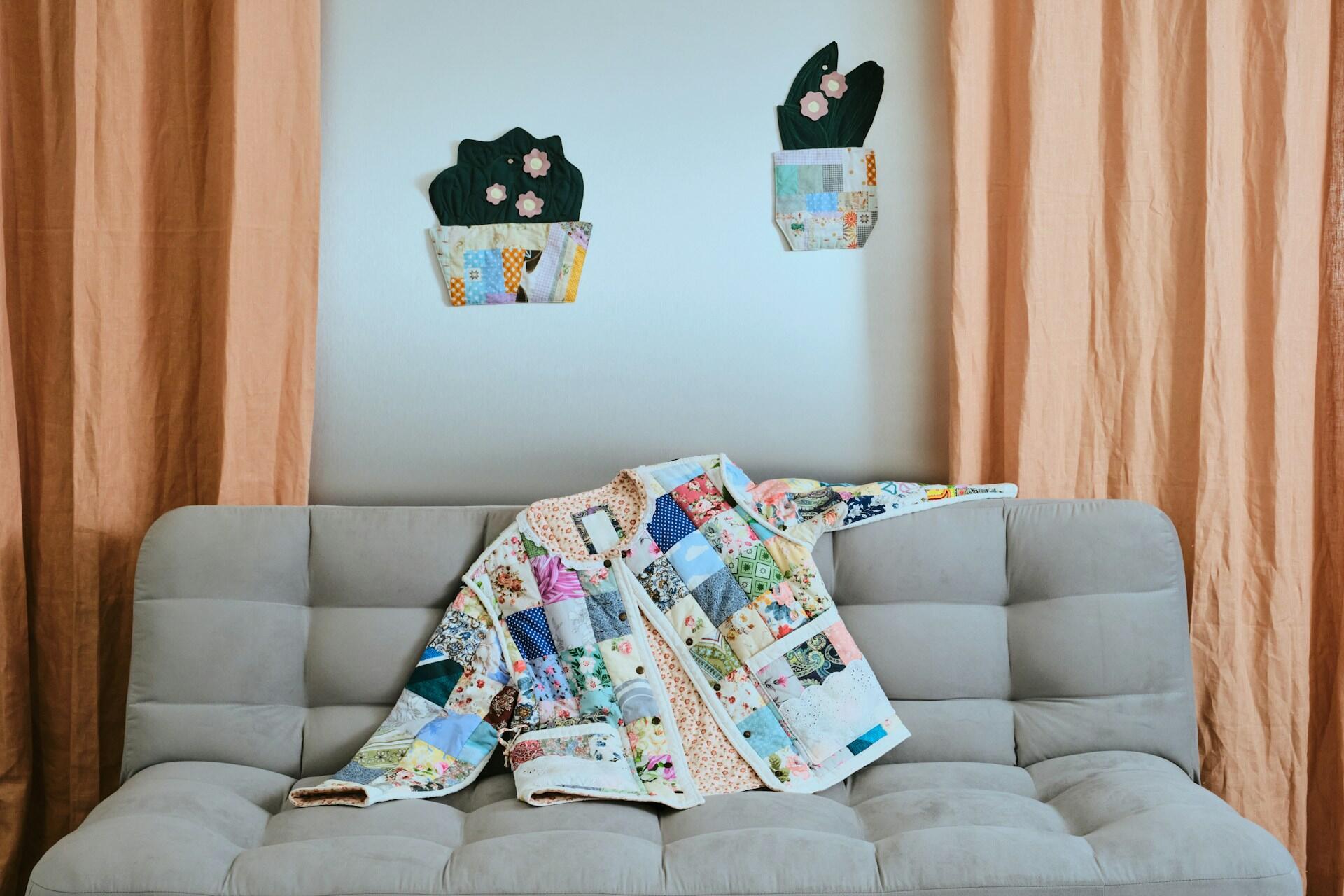 A patchwork quilted coat and decorative quilted wall hangings that look like cactuses with applique flowers