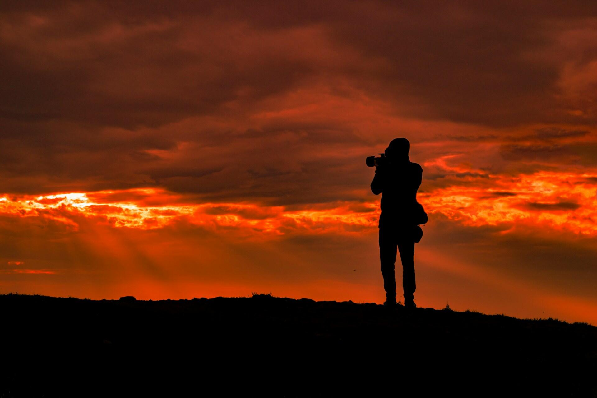 A silhouette of a photographer capturing a dramatic sunset.