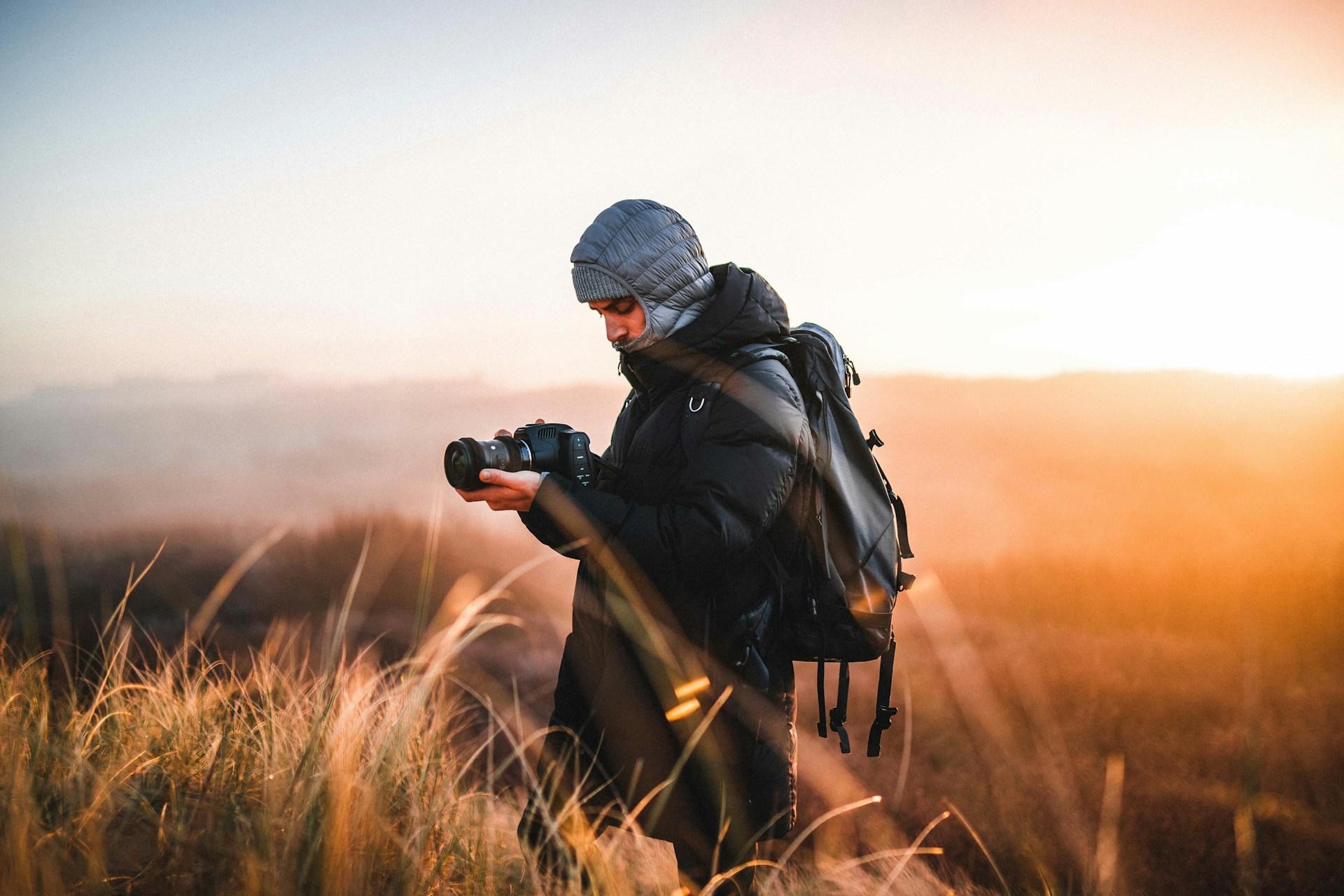 A man outdoors at sunrise holding a camera.