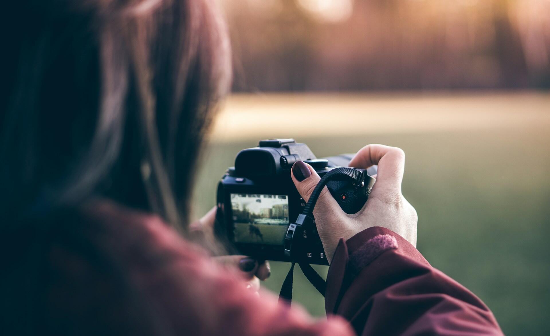 Person holding a camera, taking a photo with a blurred green background.