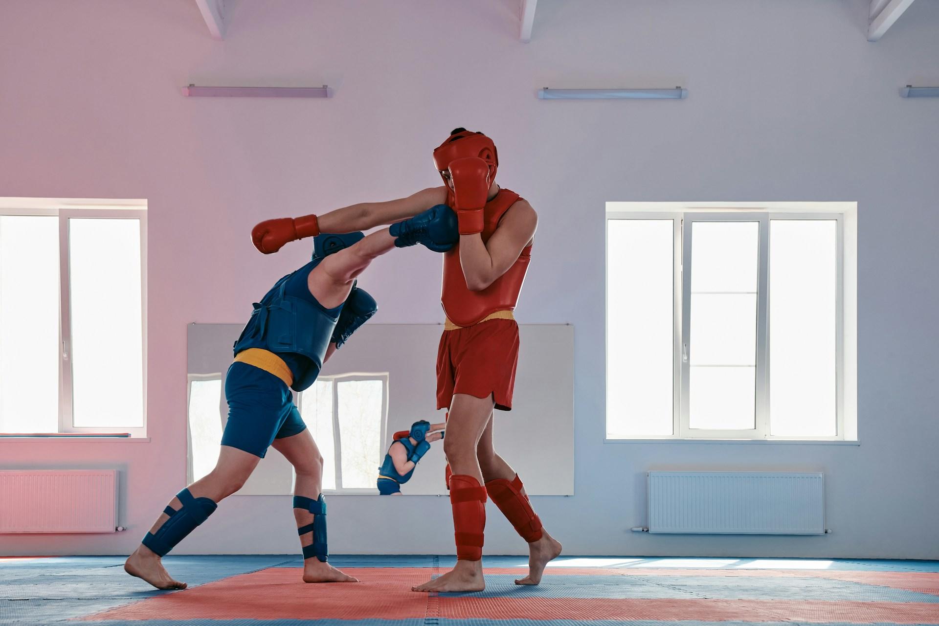 Two men in boxing gear sparring in an indoor gym.