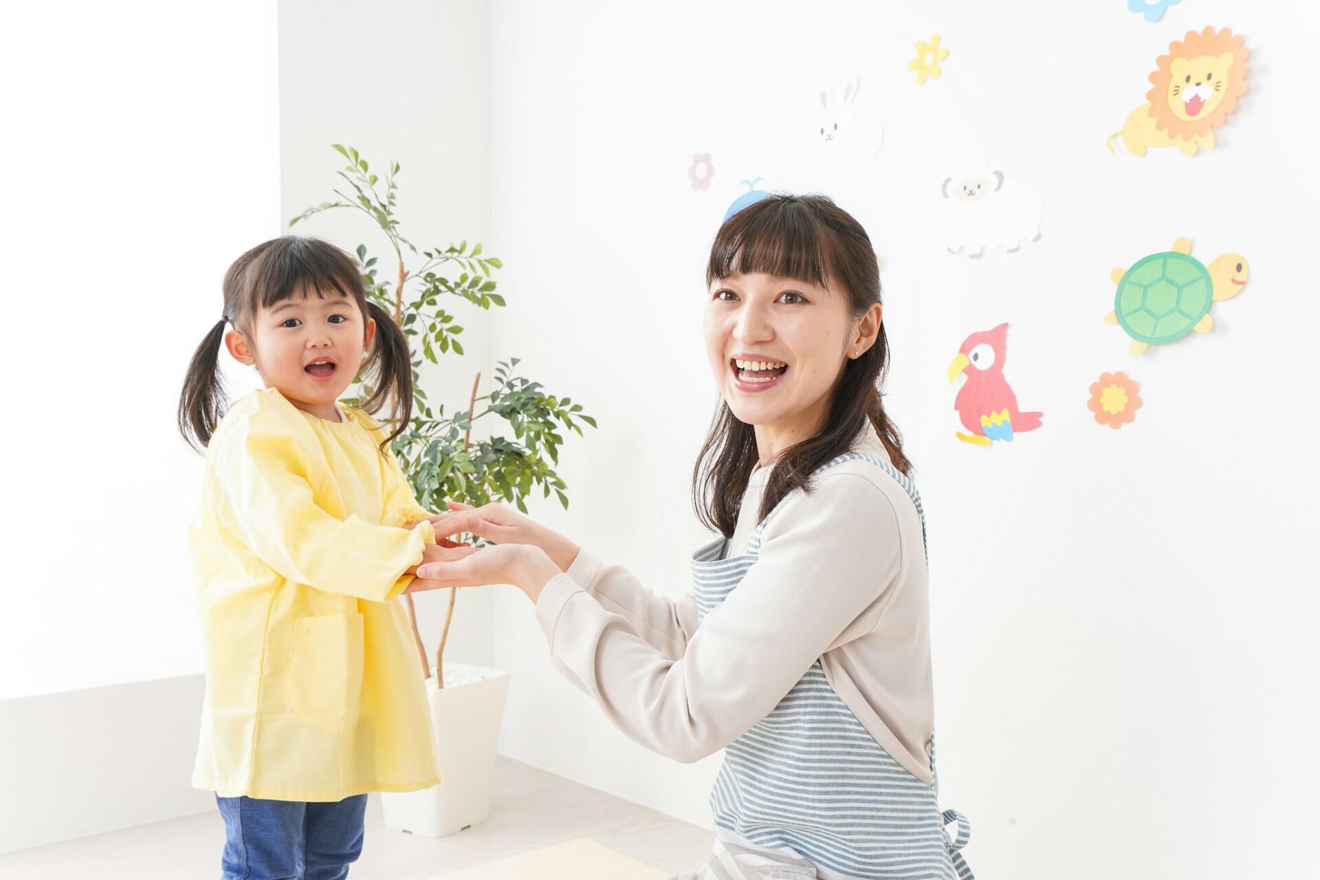 A young girl in a yellow shirt reaches out to an adult, surrounded by colorful animal decals on a white wall.