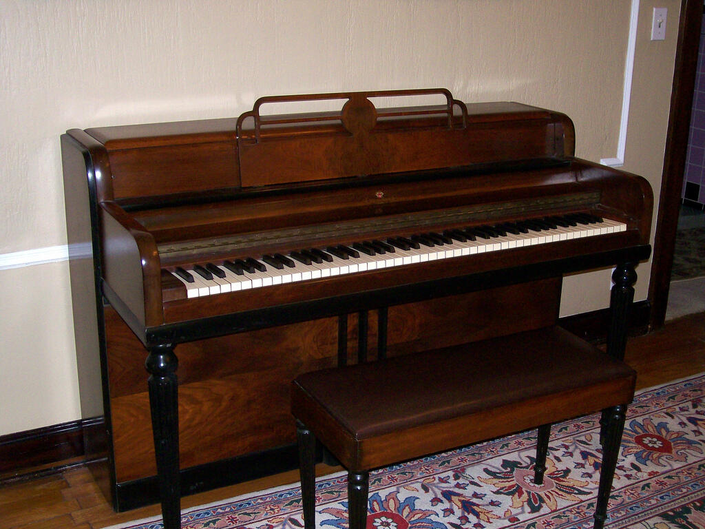 A brown spinet piano with bench. 