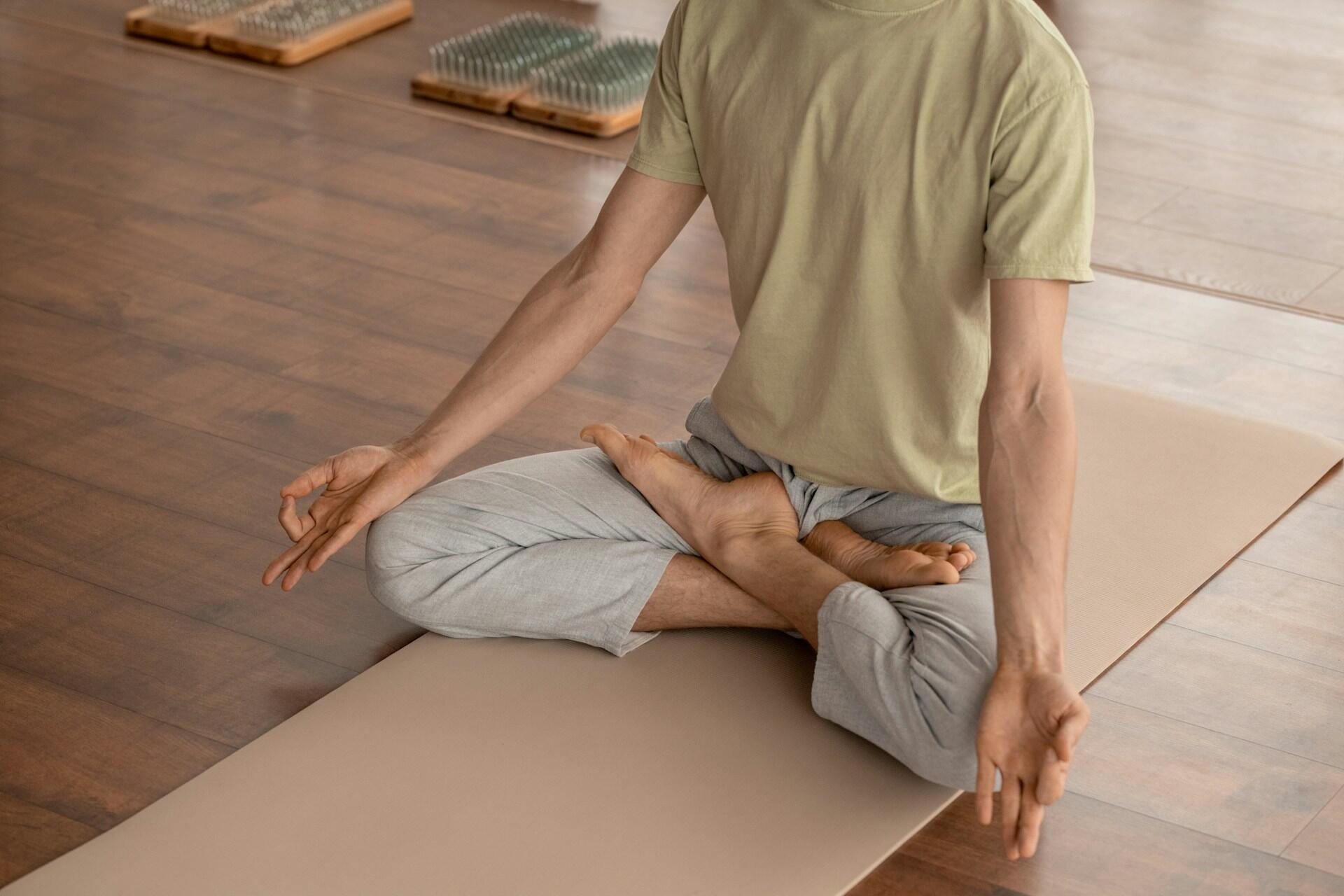 Person in a green shirt and grey pants meditating on a yoga mat.