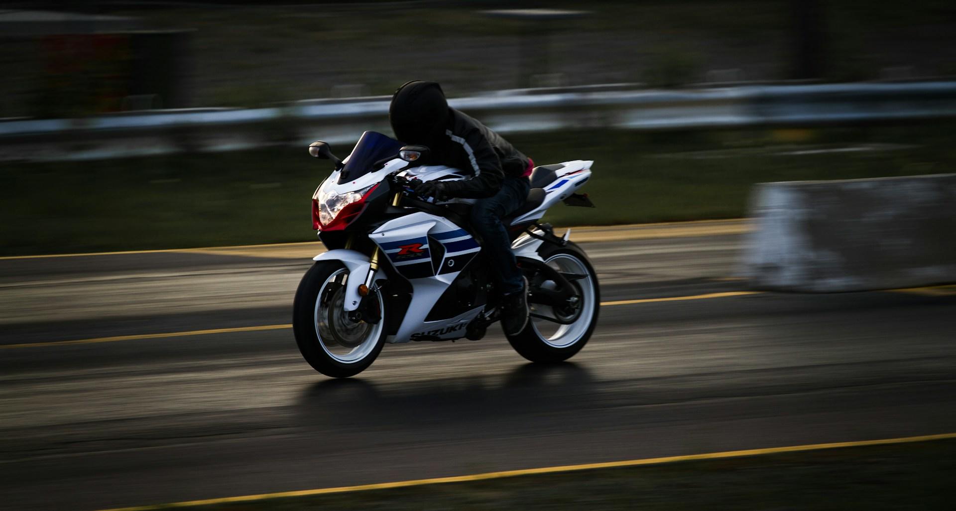 A person riding a red, black and white motorcycle speeds along a highway wearing full leathers and a black helmet.