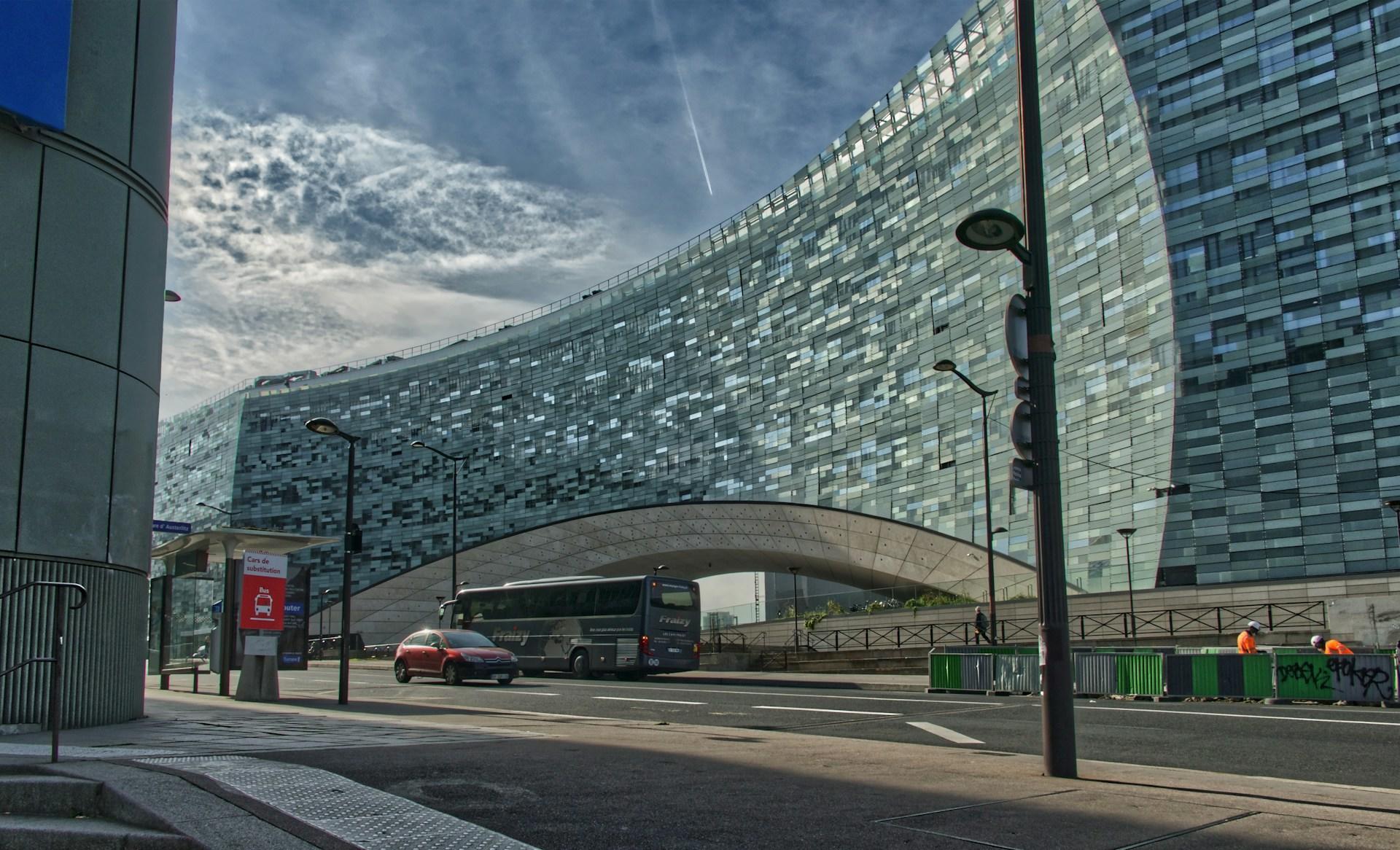 A panoramic shot of the Le Monde building in Paris, France, displaying a greenish-blue facade and featuring its iconic 'bridge', seen on a mildly cloudy day.