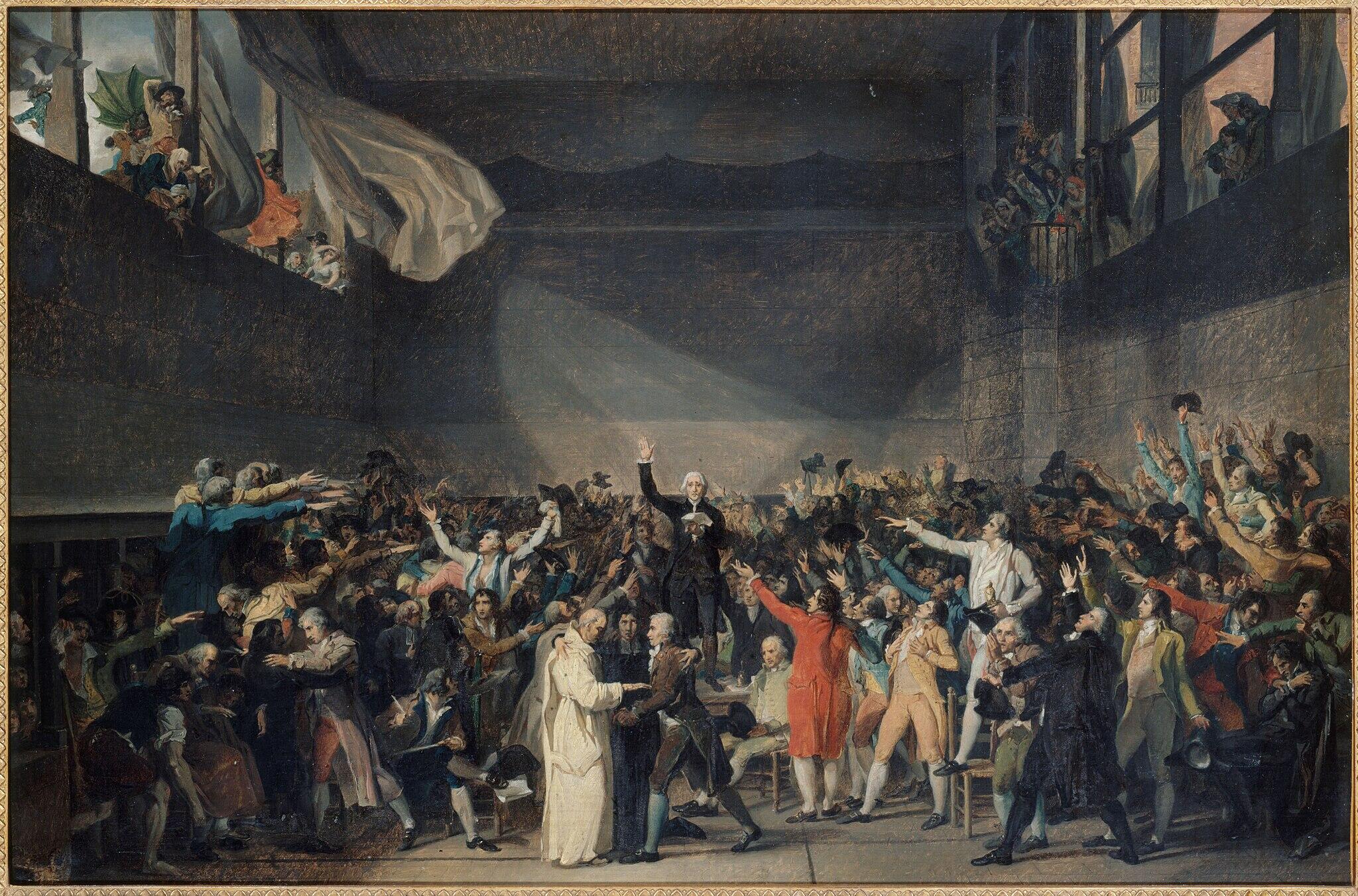 A large group of people in a room, with a man in the centre raising his hand.