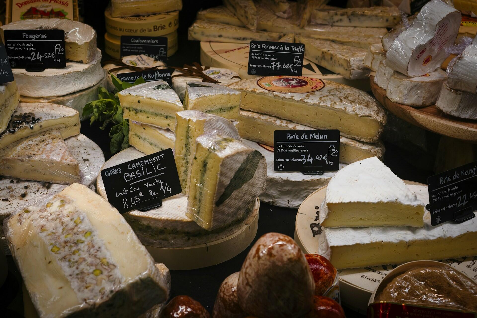 Assortment of various French cheeses on display with labels and prices.