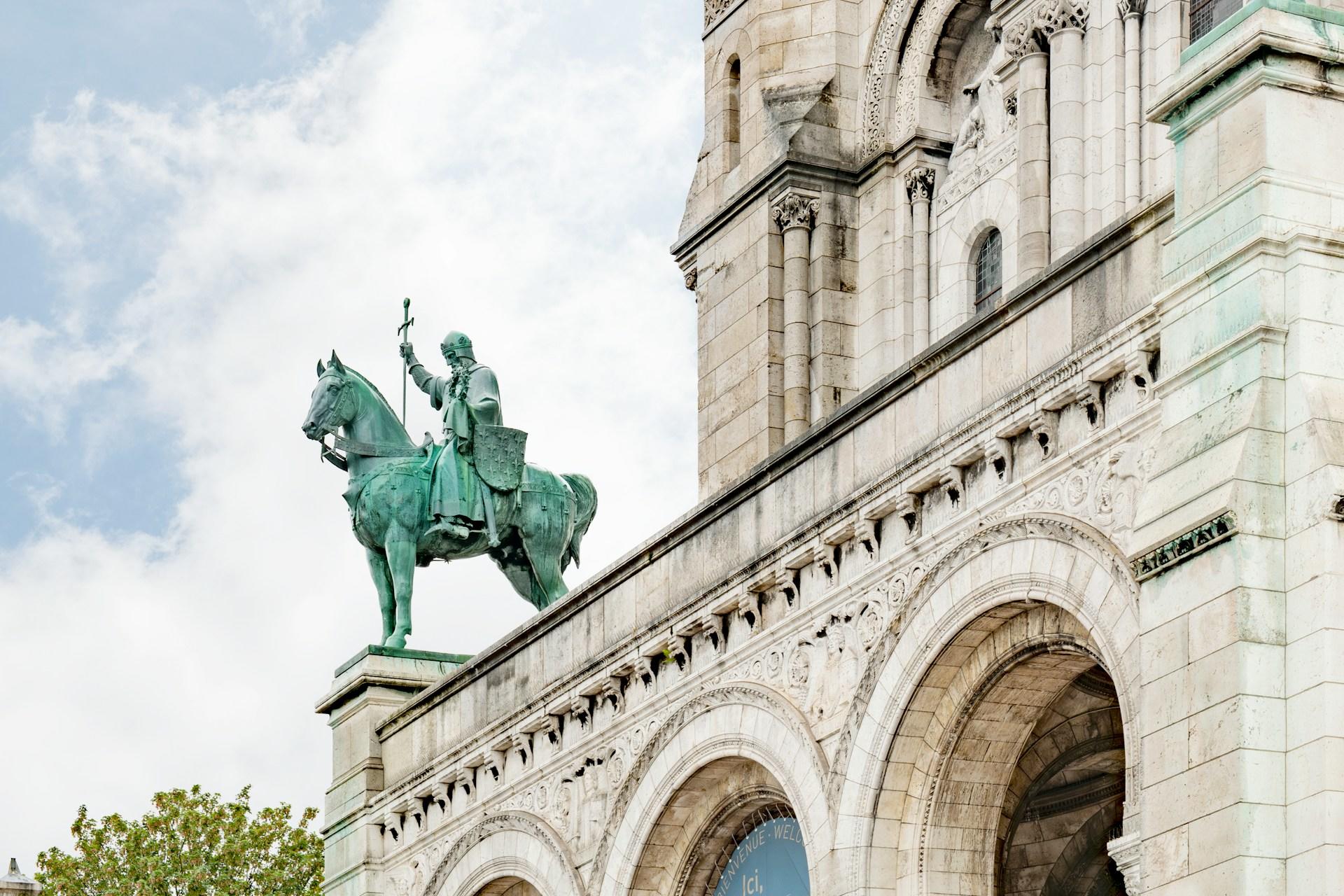 Bronze equestrian statue on a stone archway with intricate carvings and cloudy sky background.