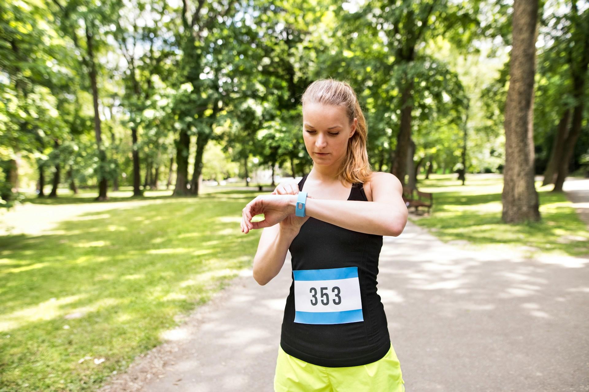 A woman running in a park, glancing at her watch to keep track of time and pace.