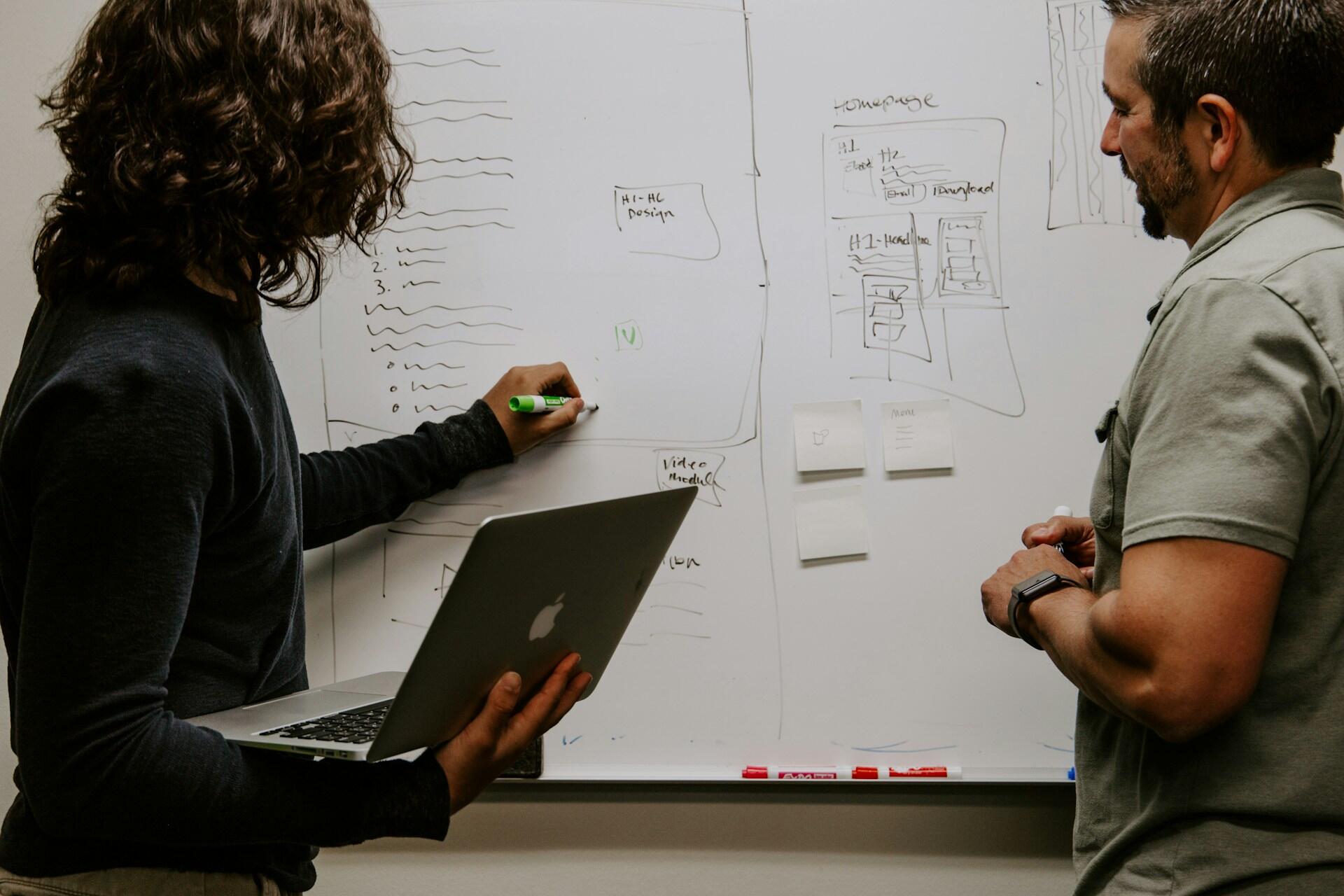 Two people studying something on a whiteboard.