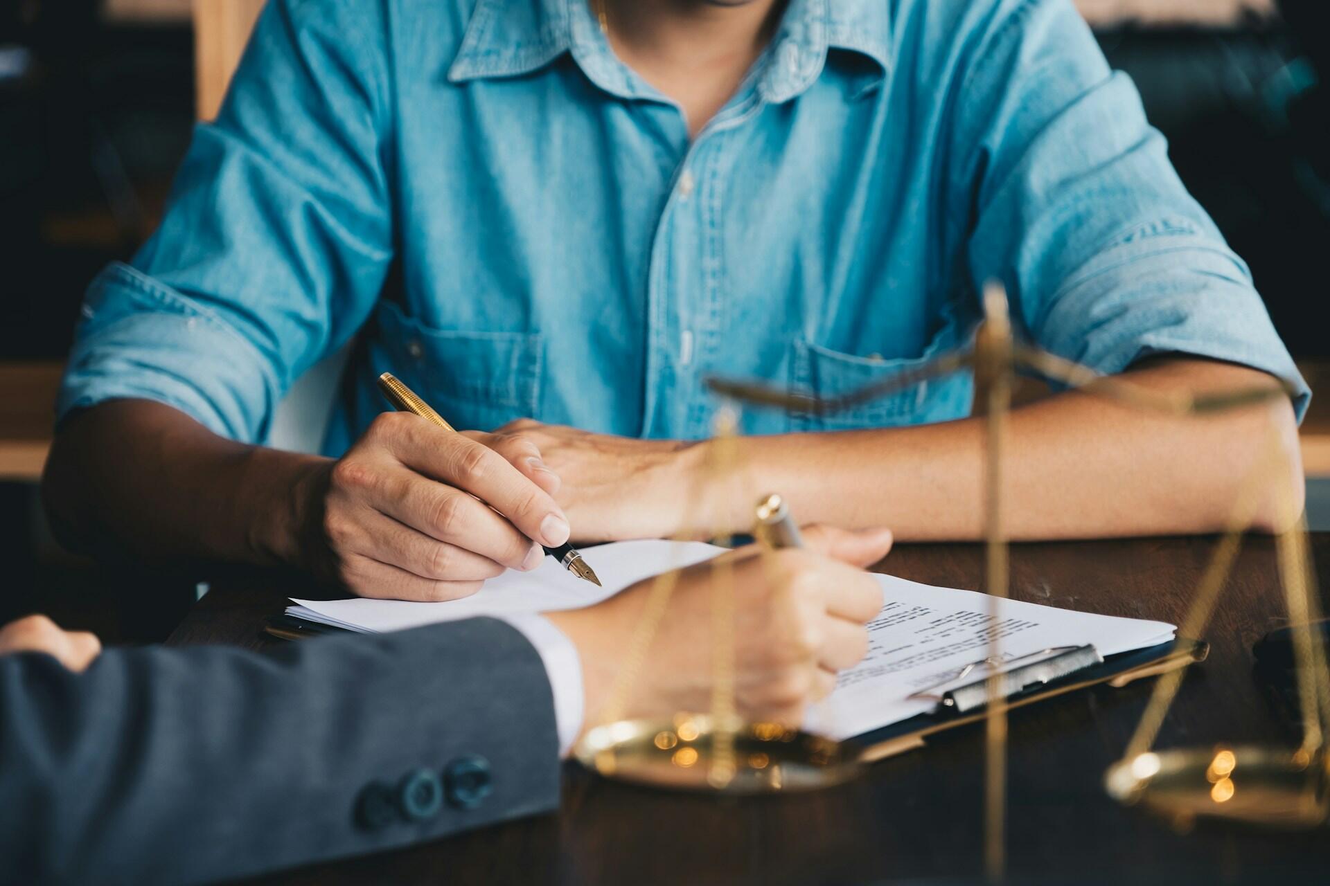 a client signing papers in a lawyer's office, with a small model of legal scales on the desk