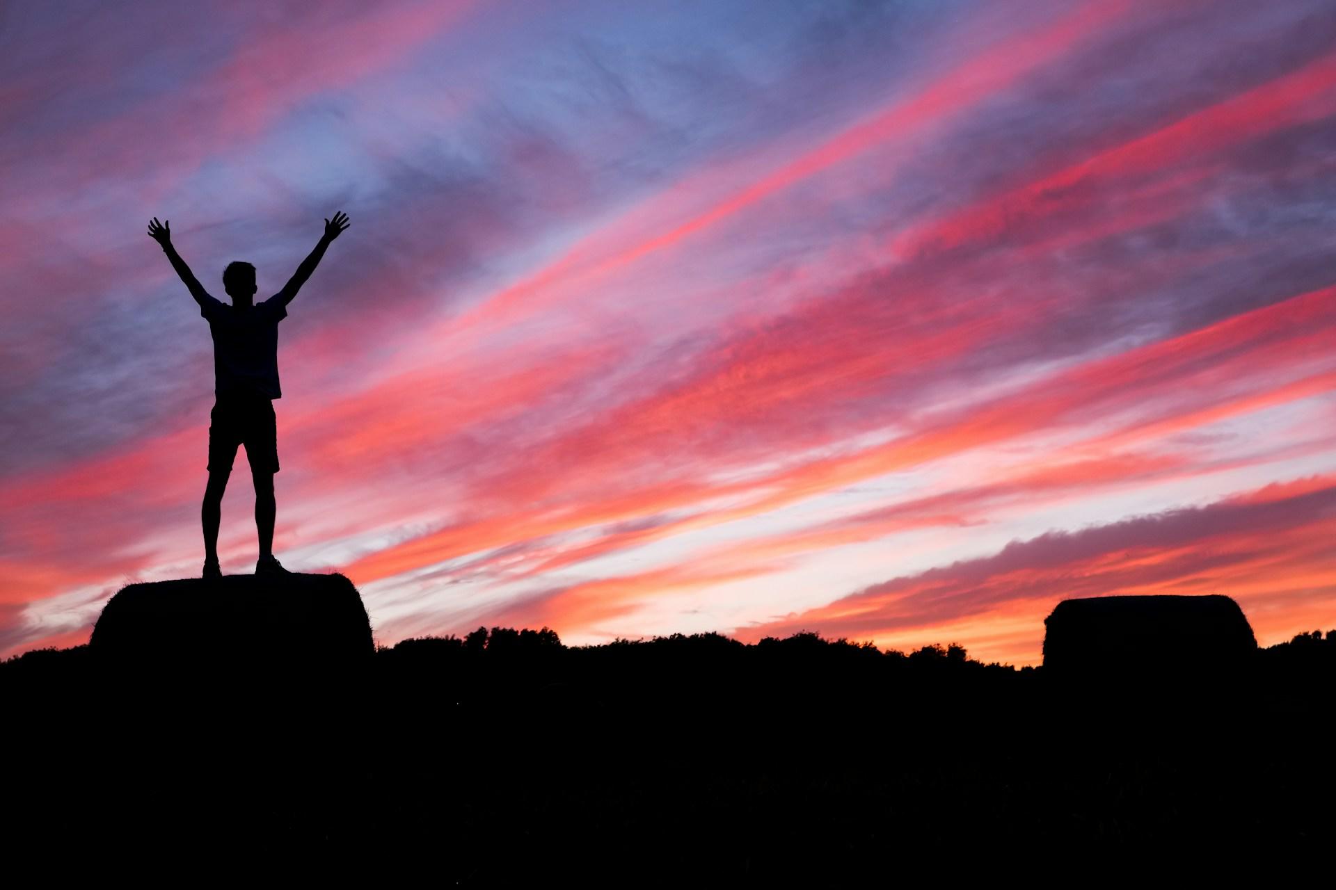 A man stands triumphantly on a rock, silhouetted against a vibrant sunset sky.