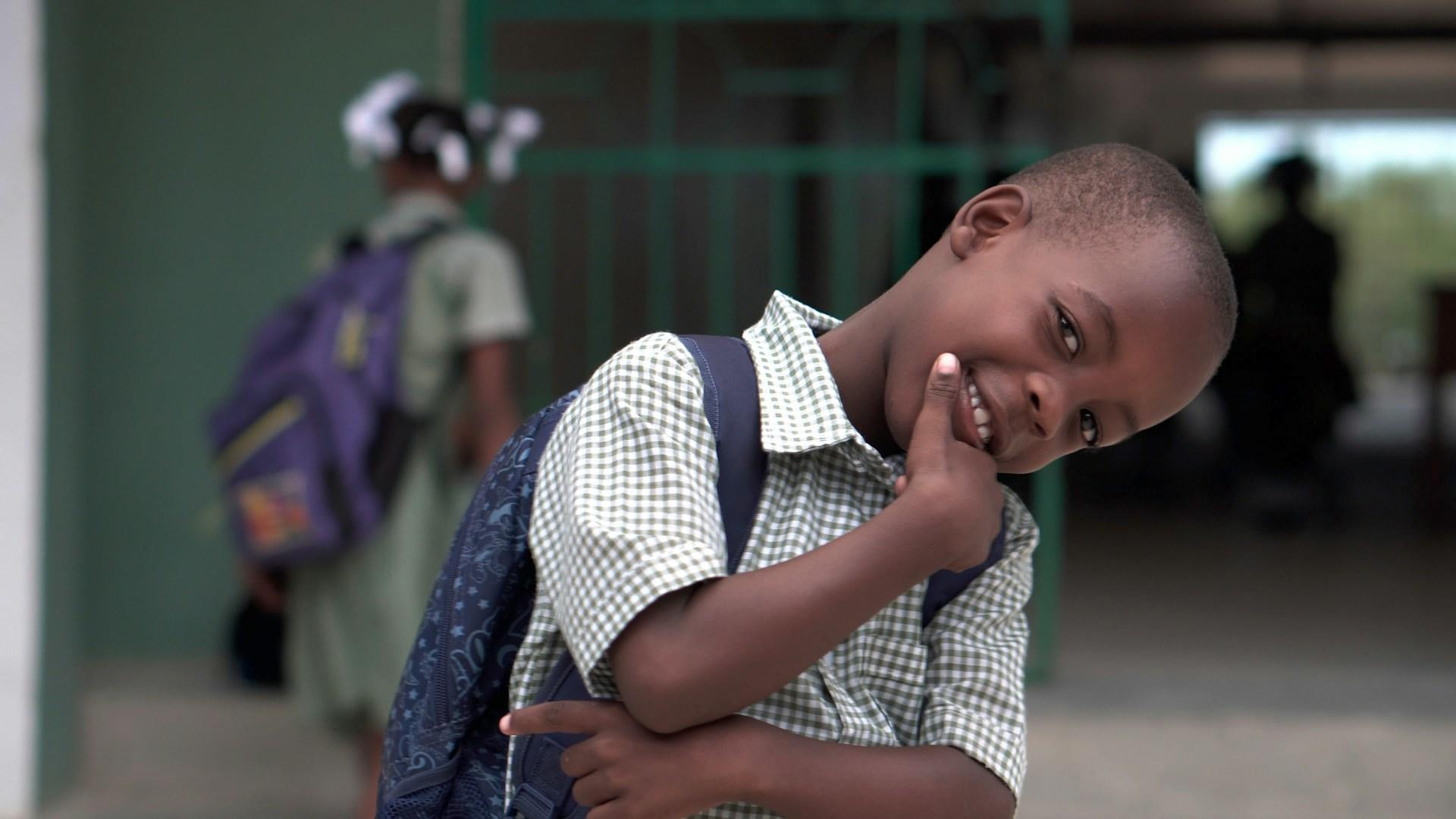a cheerful looking young boy with his hand on his chin.
