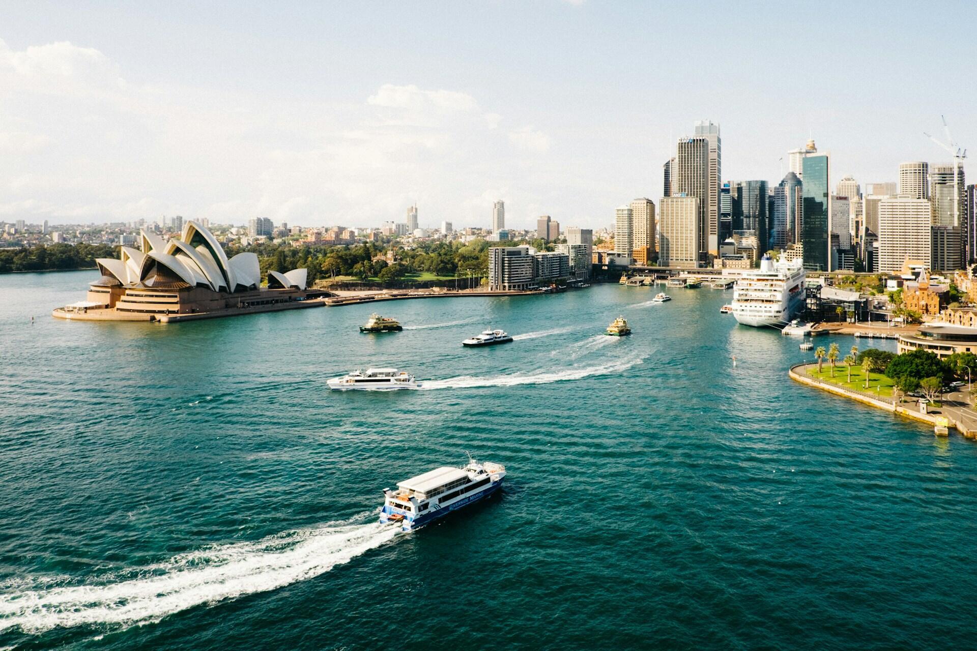 Sydney Harbour with the opera house and city buildings in the background, with the park and greenspaces between, and boats in the water
