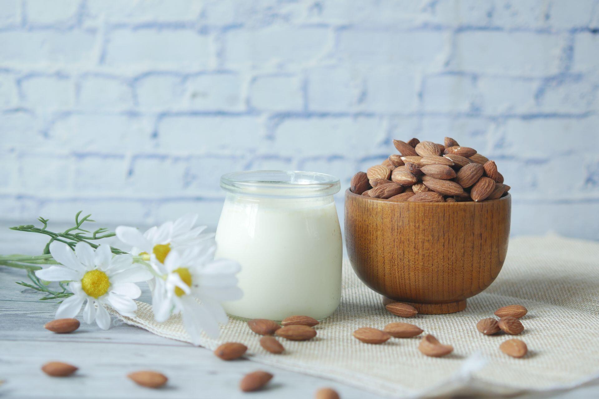 a small bowl of almonds next to a small glass of almond milk