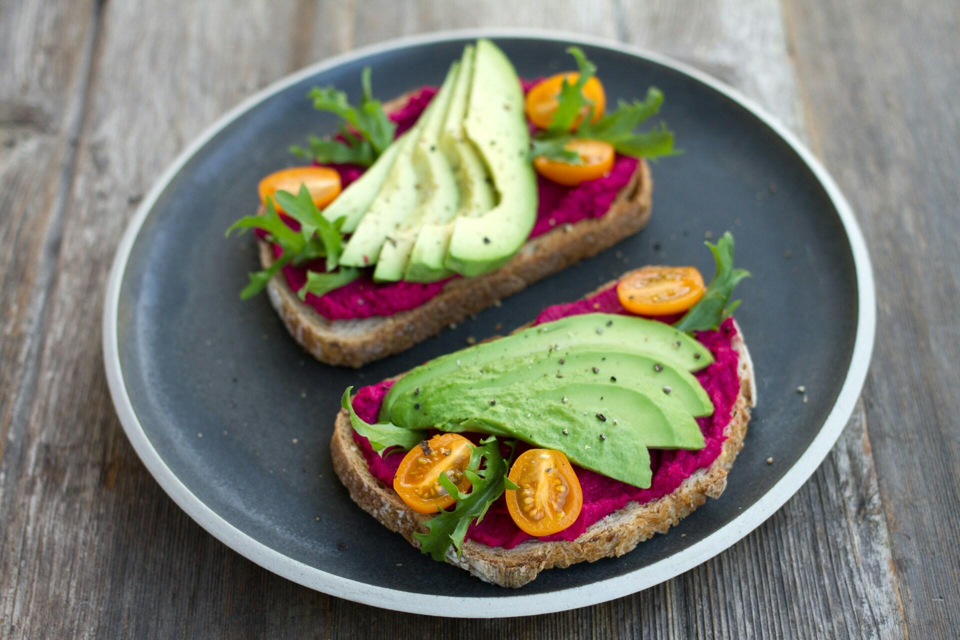 multigrain toast with beet spread, tomato slices, lettuce, and avocado slices on a ceramic plate
