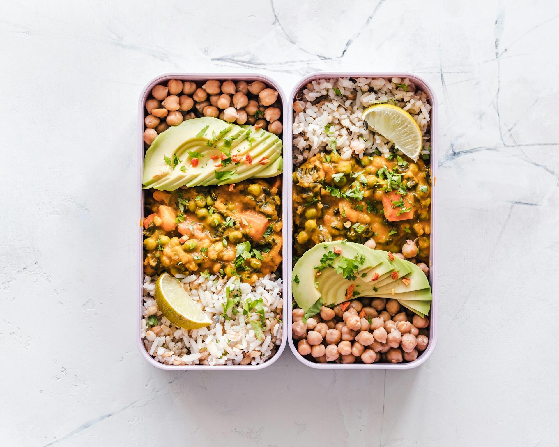 meal tins with rice, chickpeas, vegetable curry, avocado and lemon wedges, demonstrating a plant-based meal with protein