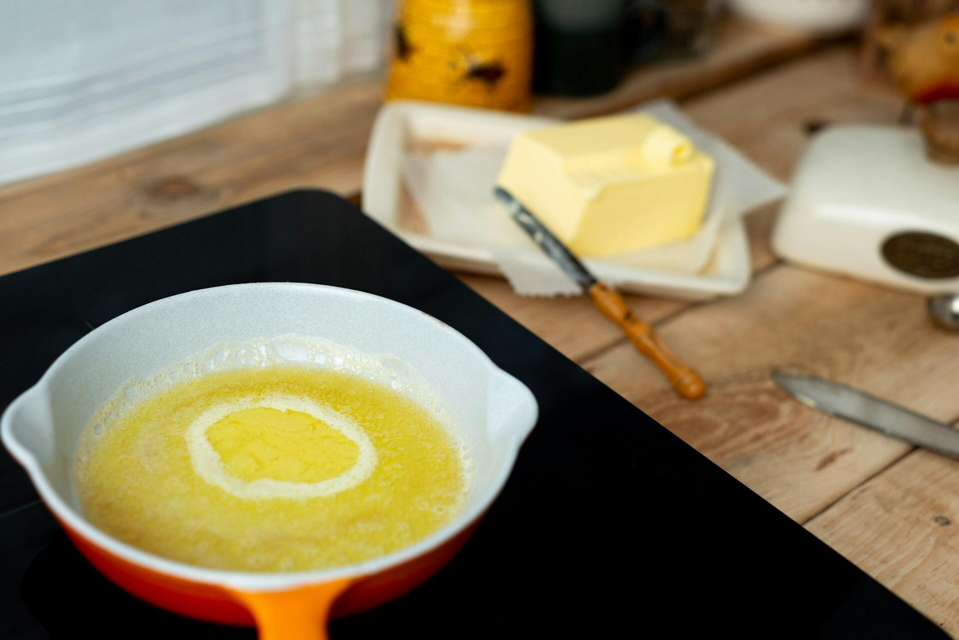 skillet on a stove top with melted butter, stick of room-temperature butter on the counter beside