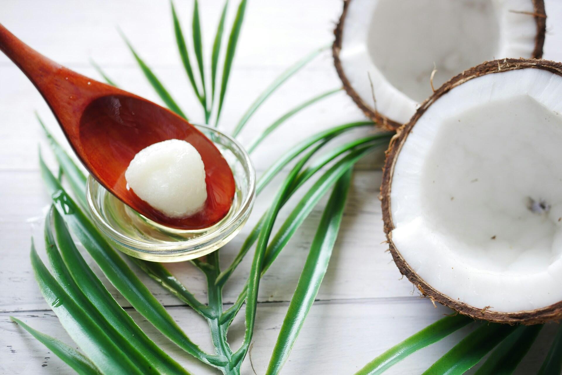 split coconut with a small bowl of coconut oil in both solid and liquid form being stirred by a wooden spoon