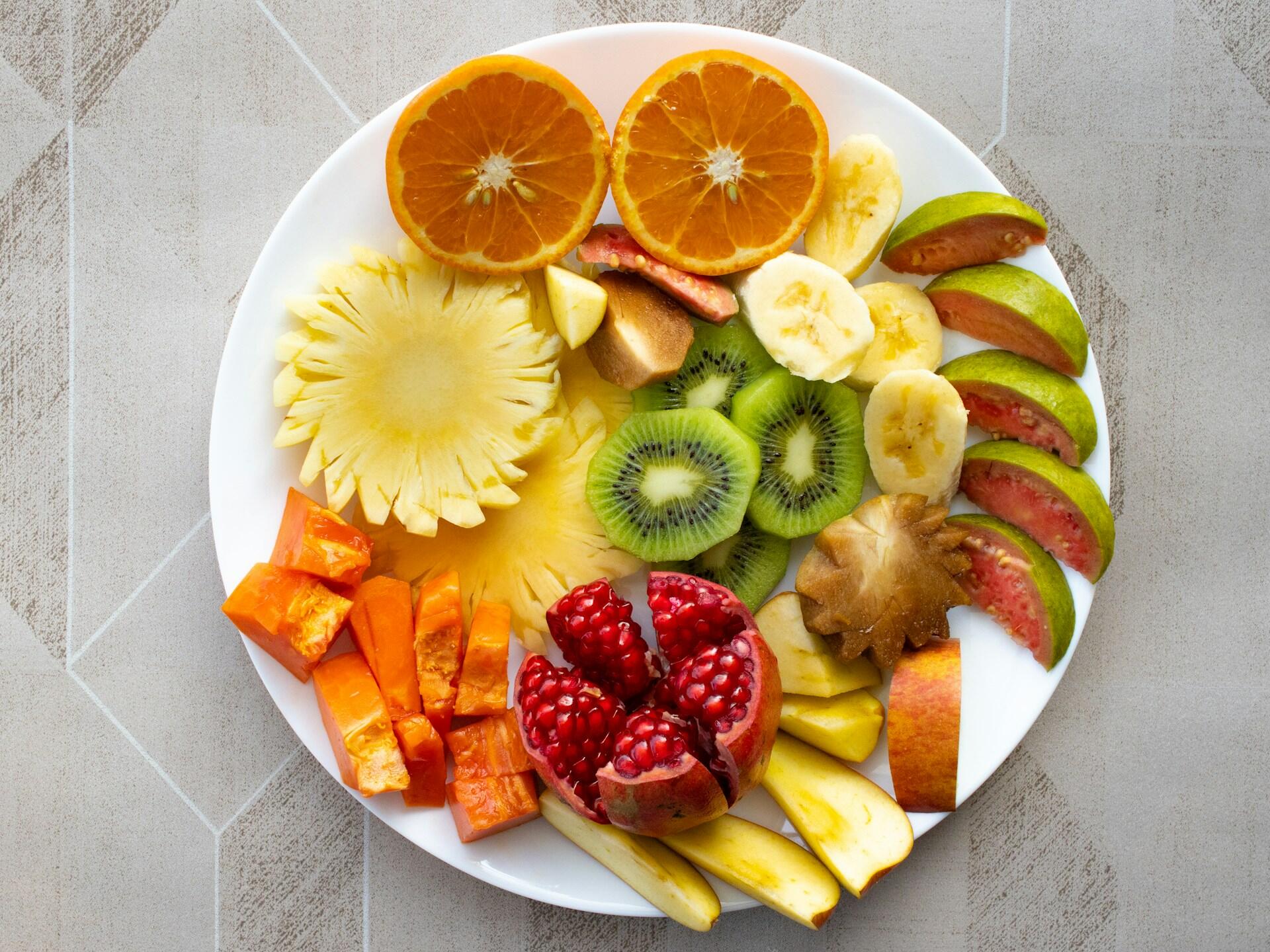 plate with small amounts of different fruits, including pineapple, peppers, pomegranate, apple, kiwi, orange, banana, and guava