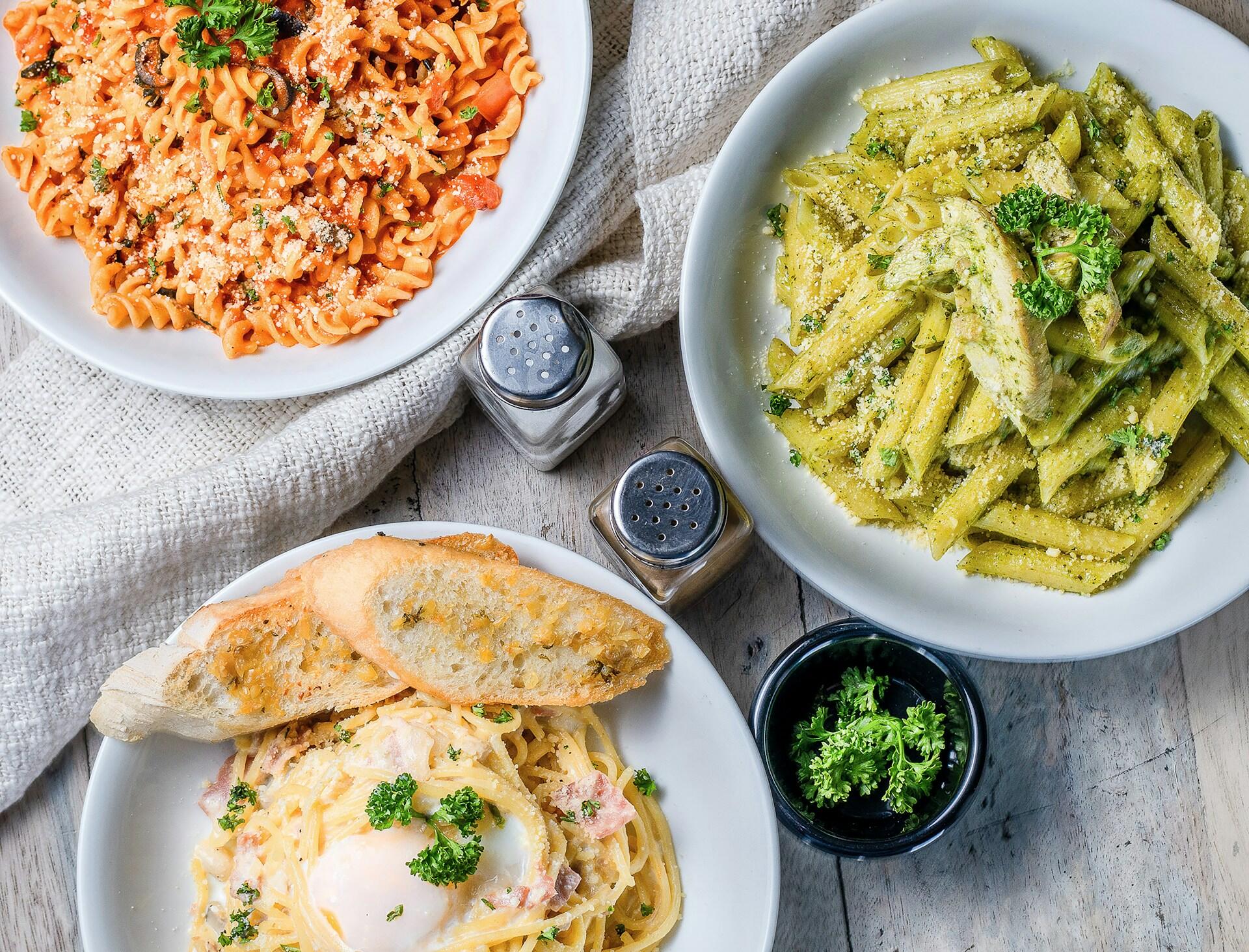 three different pasta dishes. One has marinara sauce, one has pesto sauce, and one has Alfredo sauce.