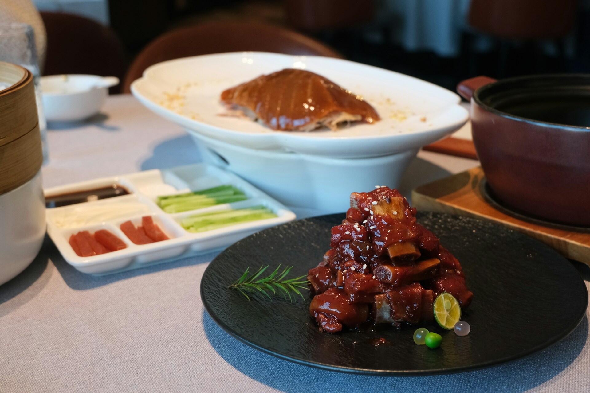 A plate of braised ribs along with other dishes on a white surface. 
