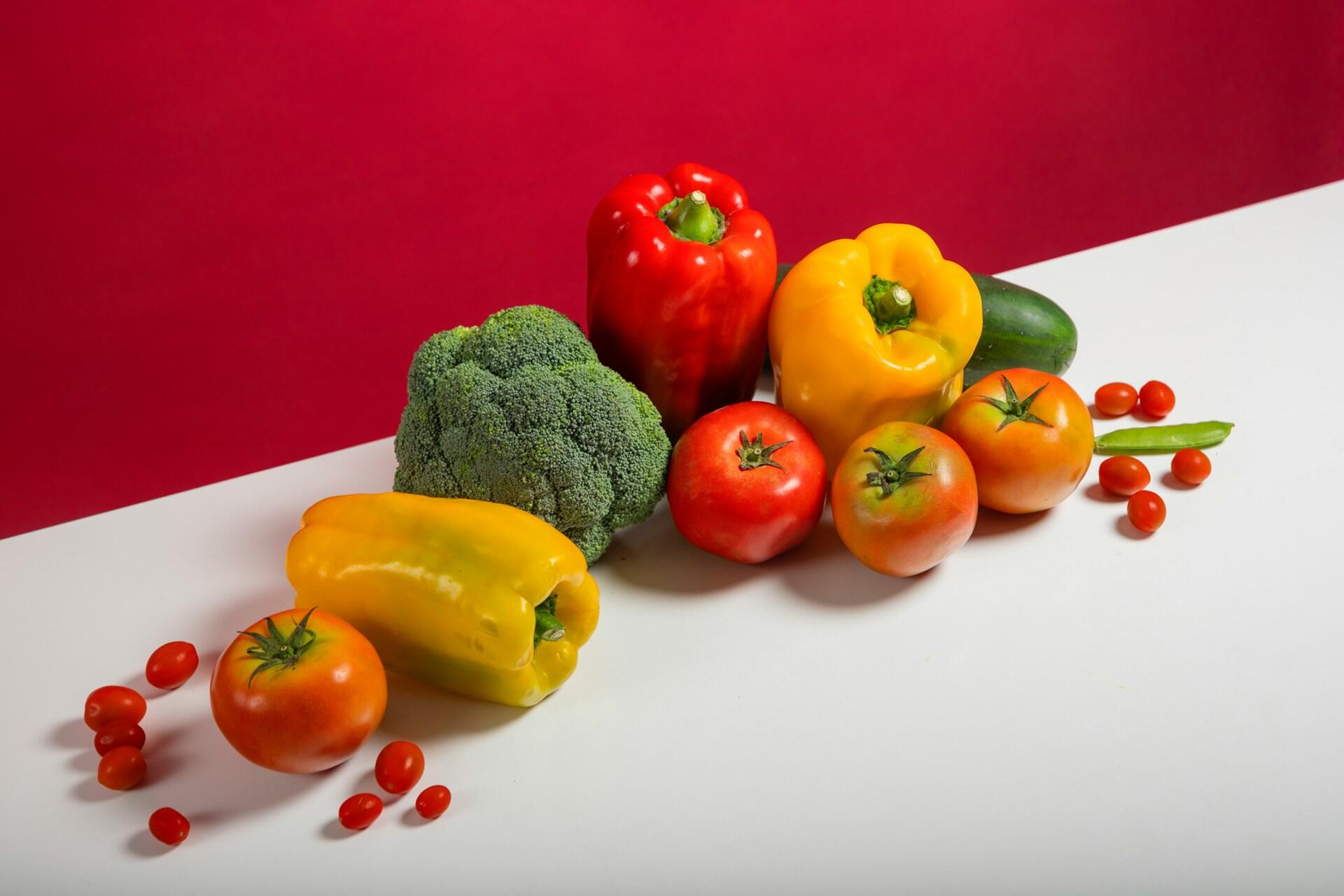 capsicum, broccoli, tomatoes, and peas on a red and white background