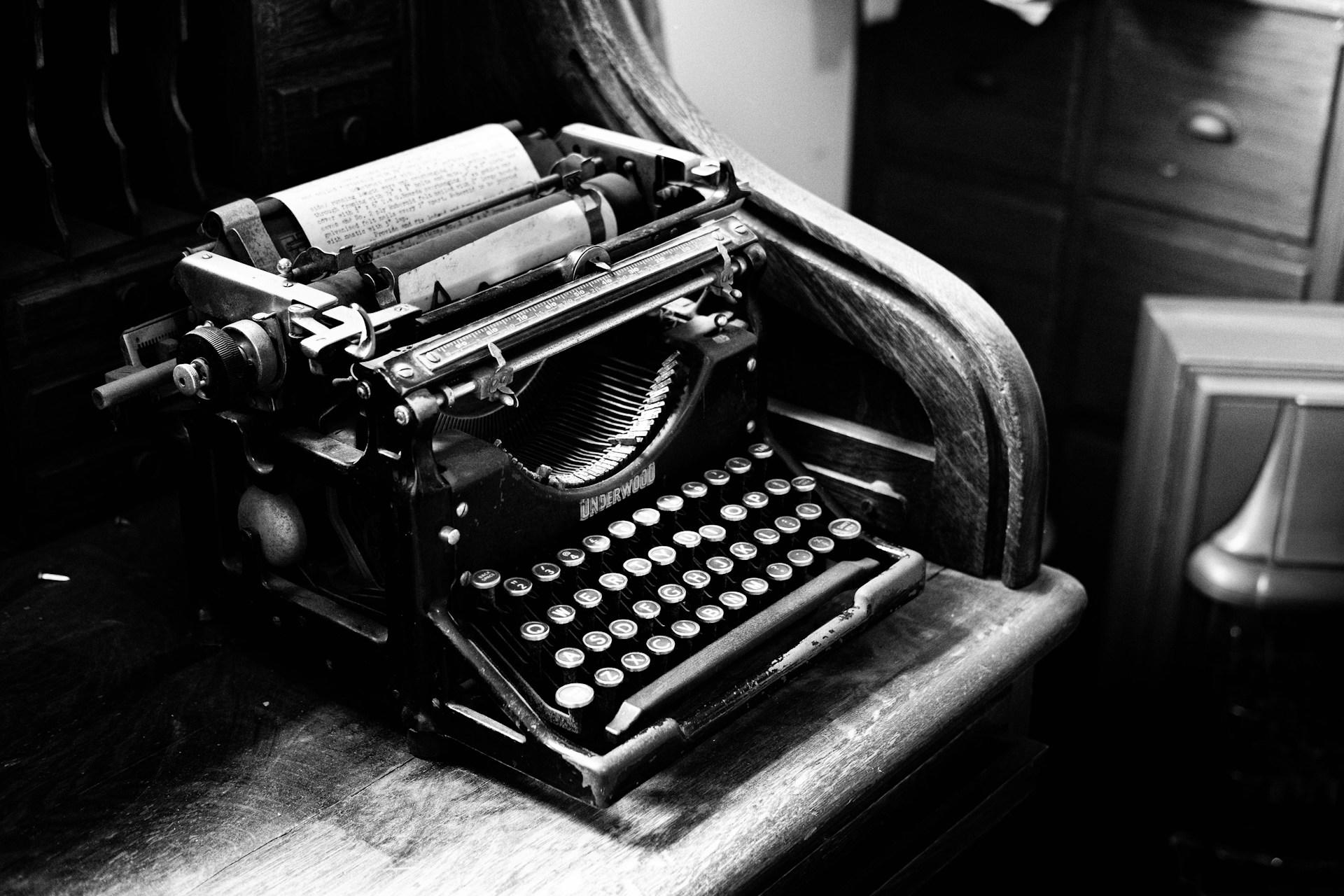 A black and white photo of a type writer on a table.