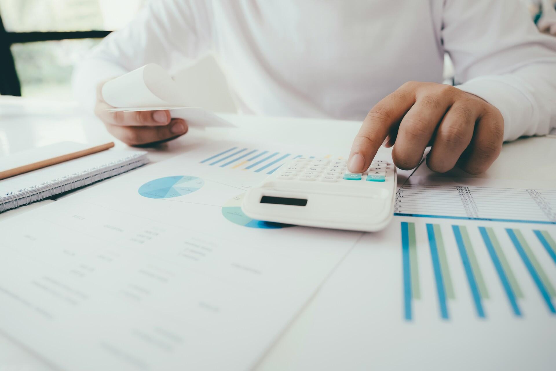 Person using a calculator over financial documents with charts and graphs.