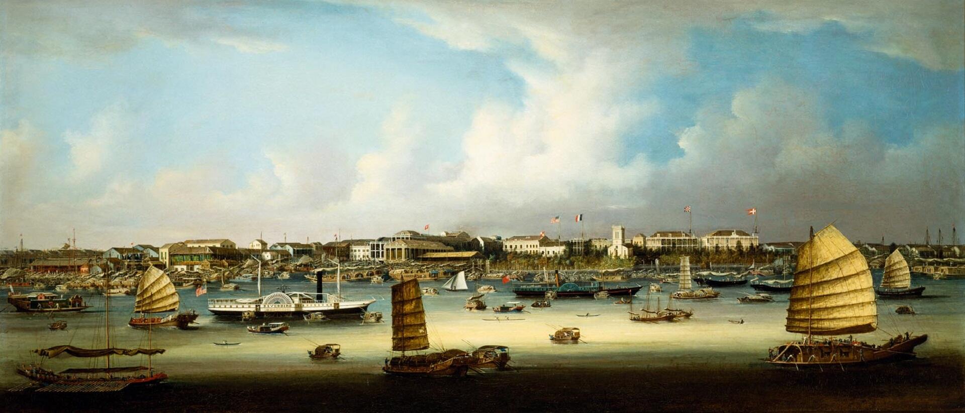 A busy commerce port with many ships in the foreground and large buildings in the background.